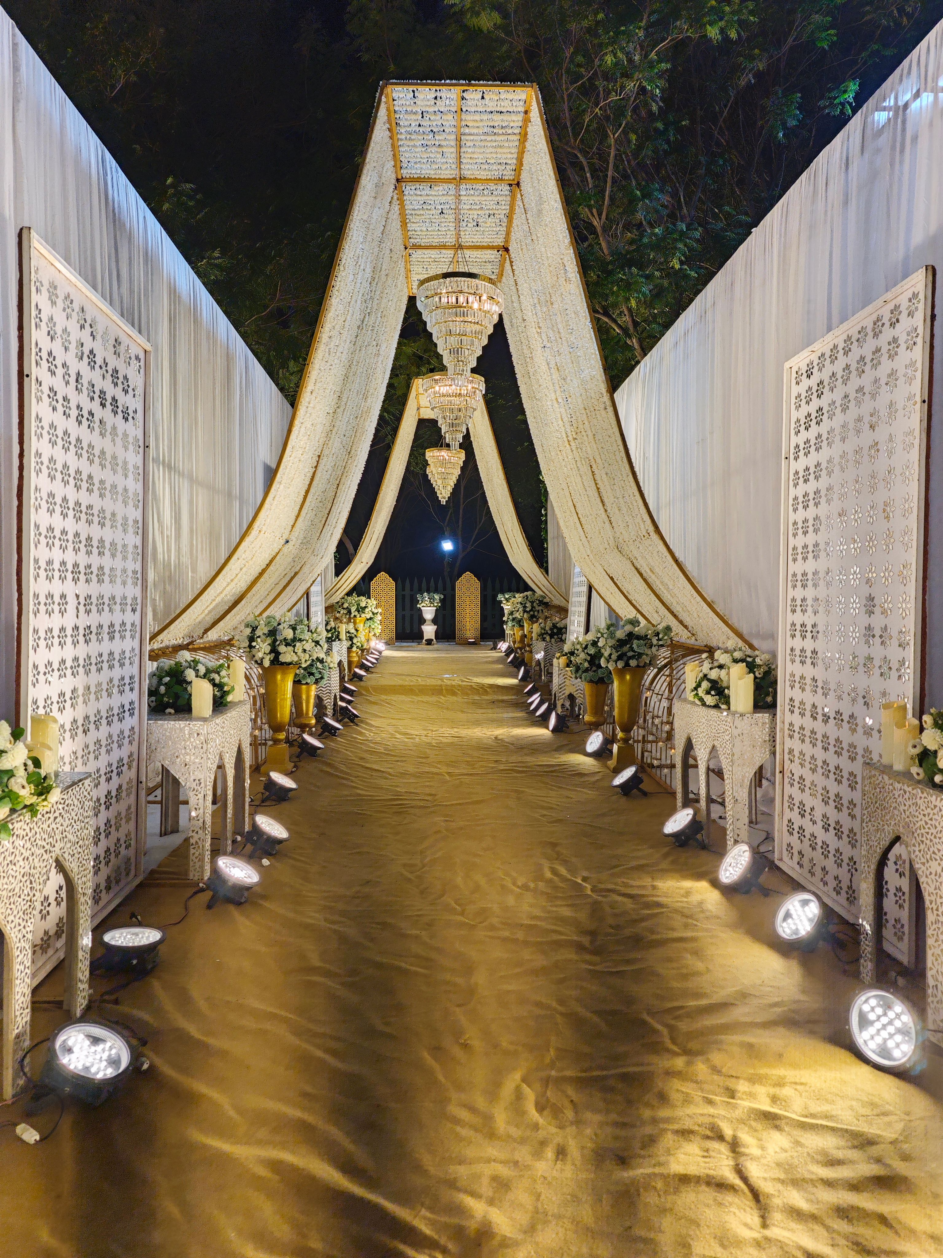 Elegant wedding aisle with chandeliers and floral arrangements under moonlight at night.