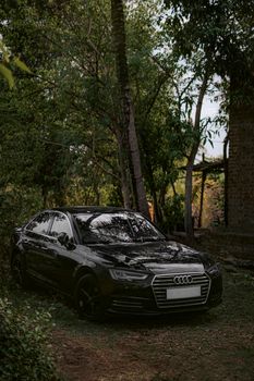 A sleek black Audi car parked amidst lush greenery in Kolhapur, India.