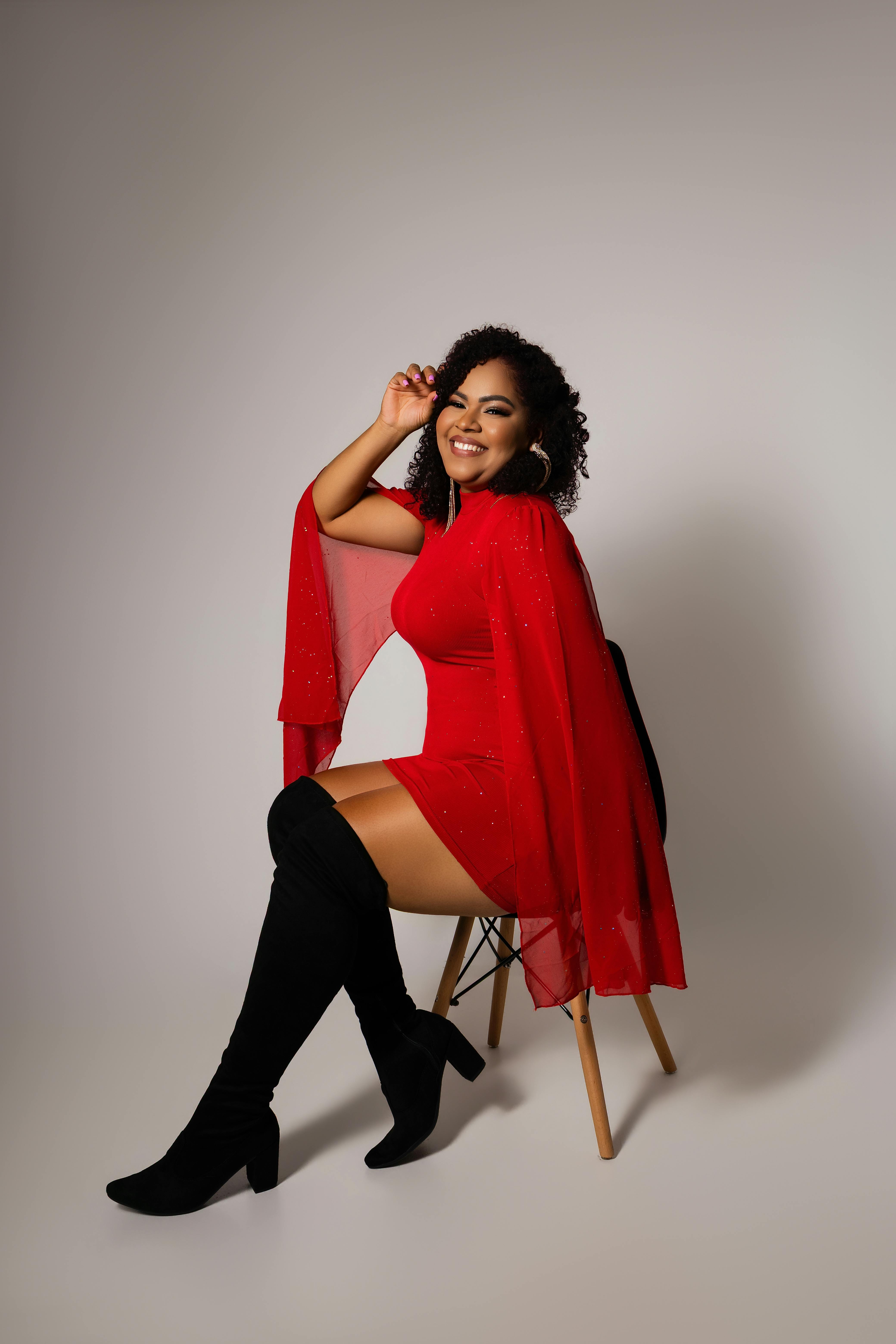De franc Dona alegre amb un vestit vermell i botes negres posant amb confiança en un entorn minimalista. Foto d'estoc