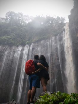 Couple standing at Tumpak Sewu Waterfall, Jawa Timur. A breathtaking moment in nature.
