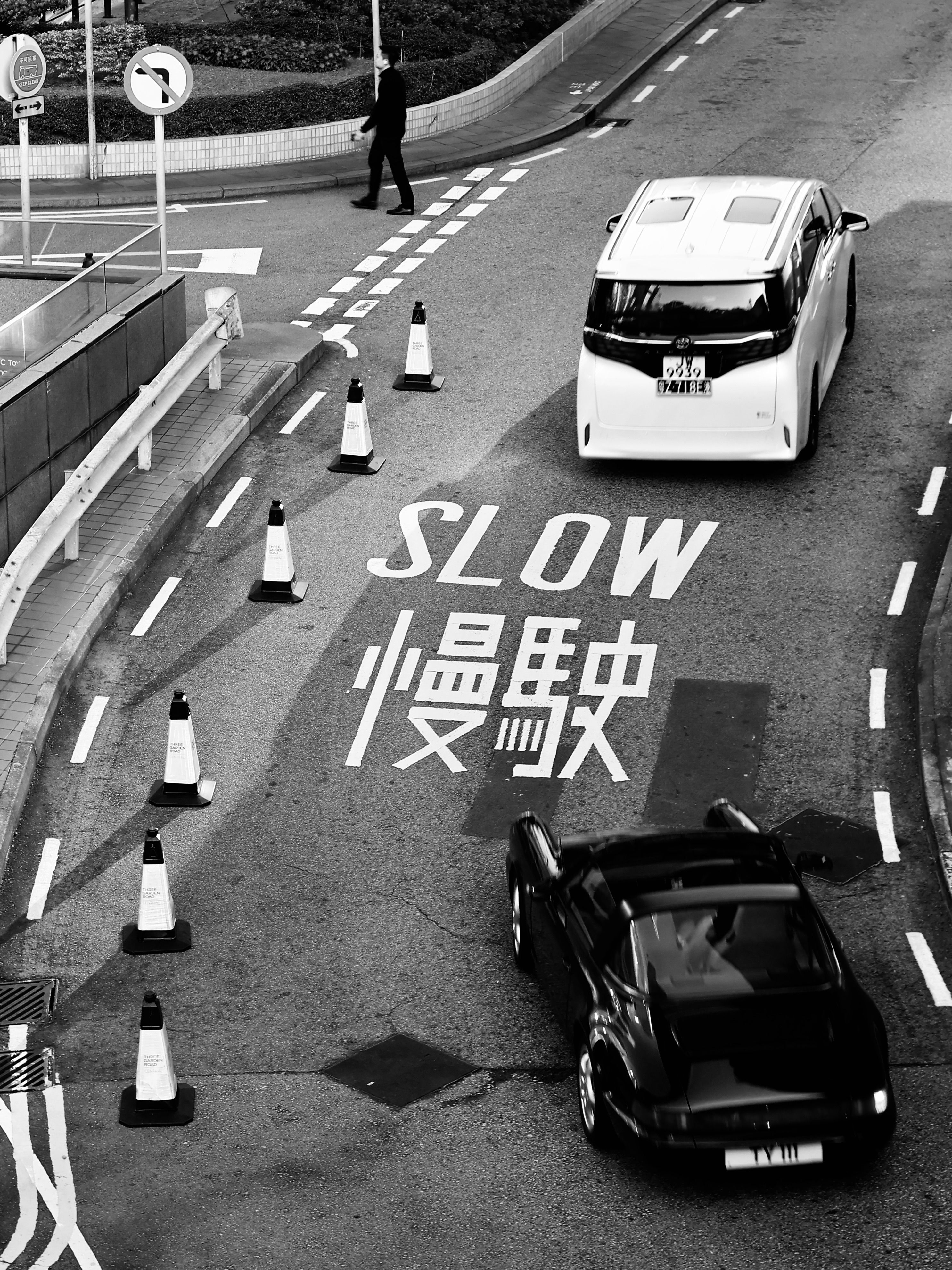 Black and white photo of urban street with 'SLOW' sign and cars. High contrast.