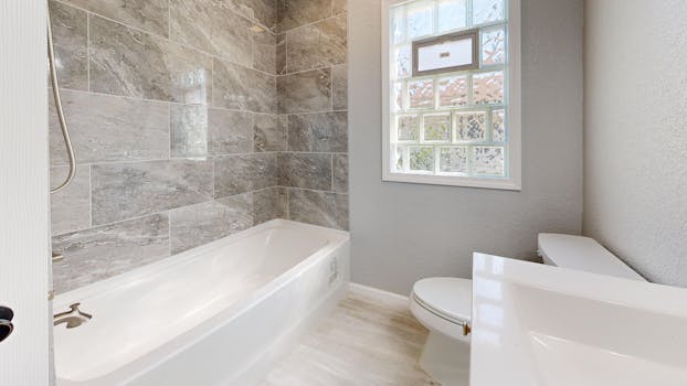 Spacious bathroom interior featuring a bathtub, sleek gray tiles, and a glass window.