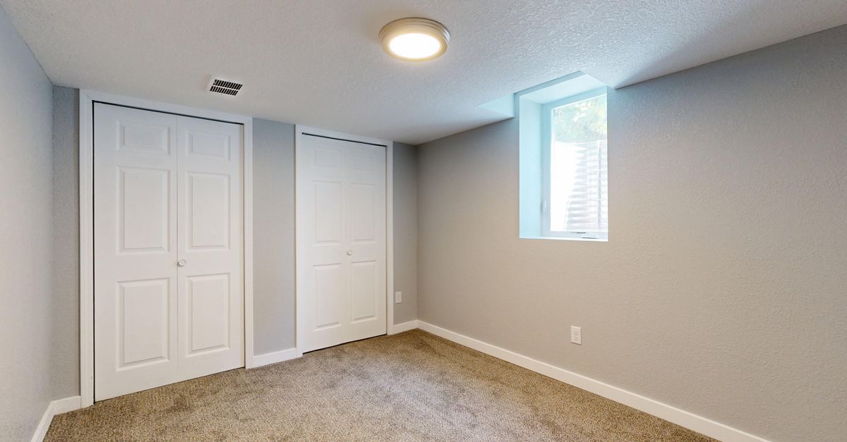 Minimalistic empty room with carpet, two white doors, and natural light from a window.