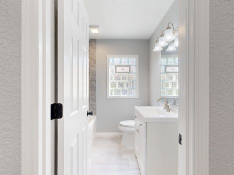 Bright and modern bathroom with white fixtures and natural light through glass window blocks.