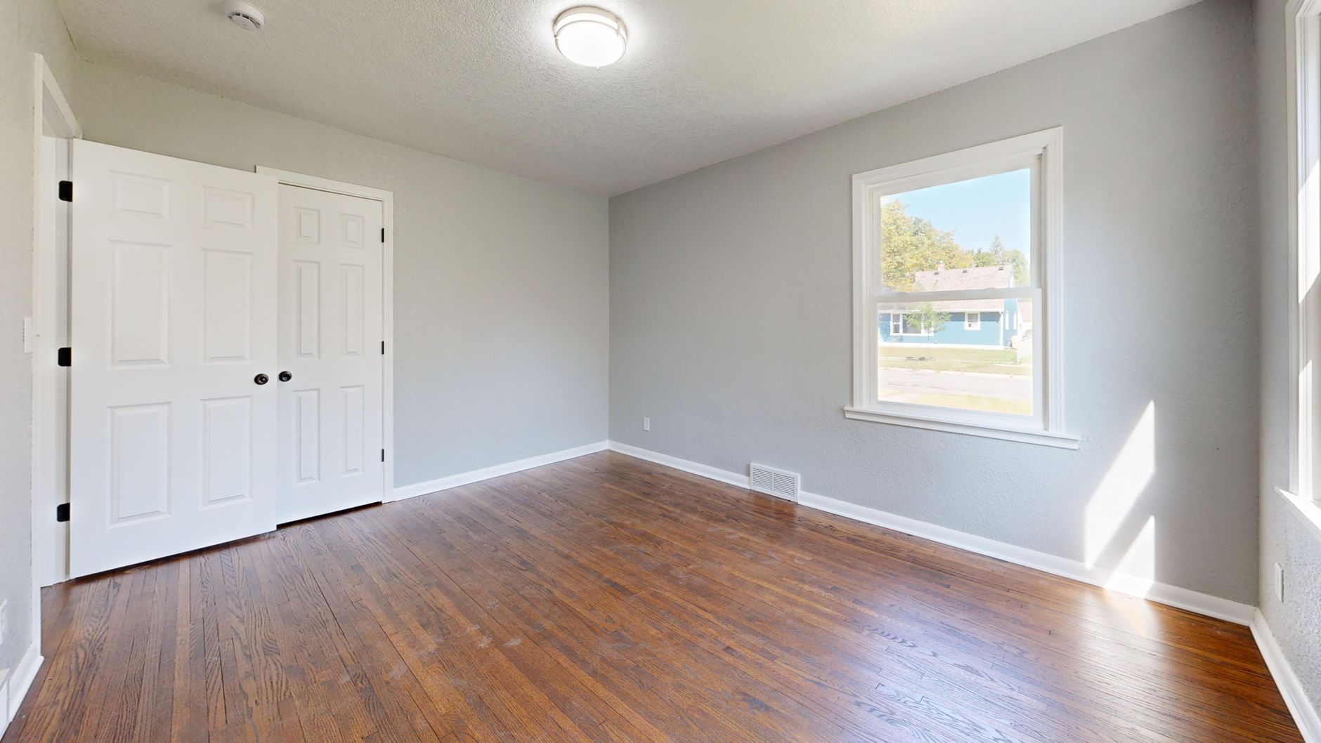 Spacious empty room with wooden flooring and natural light.