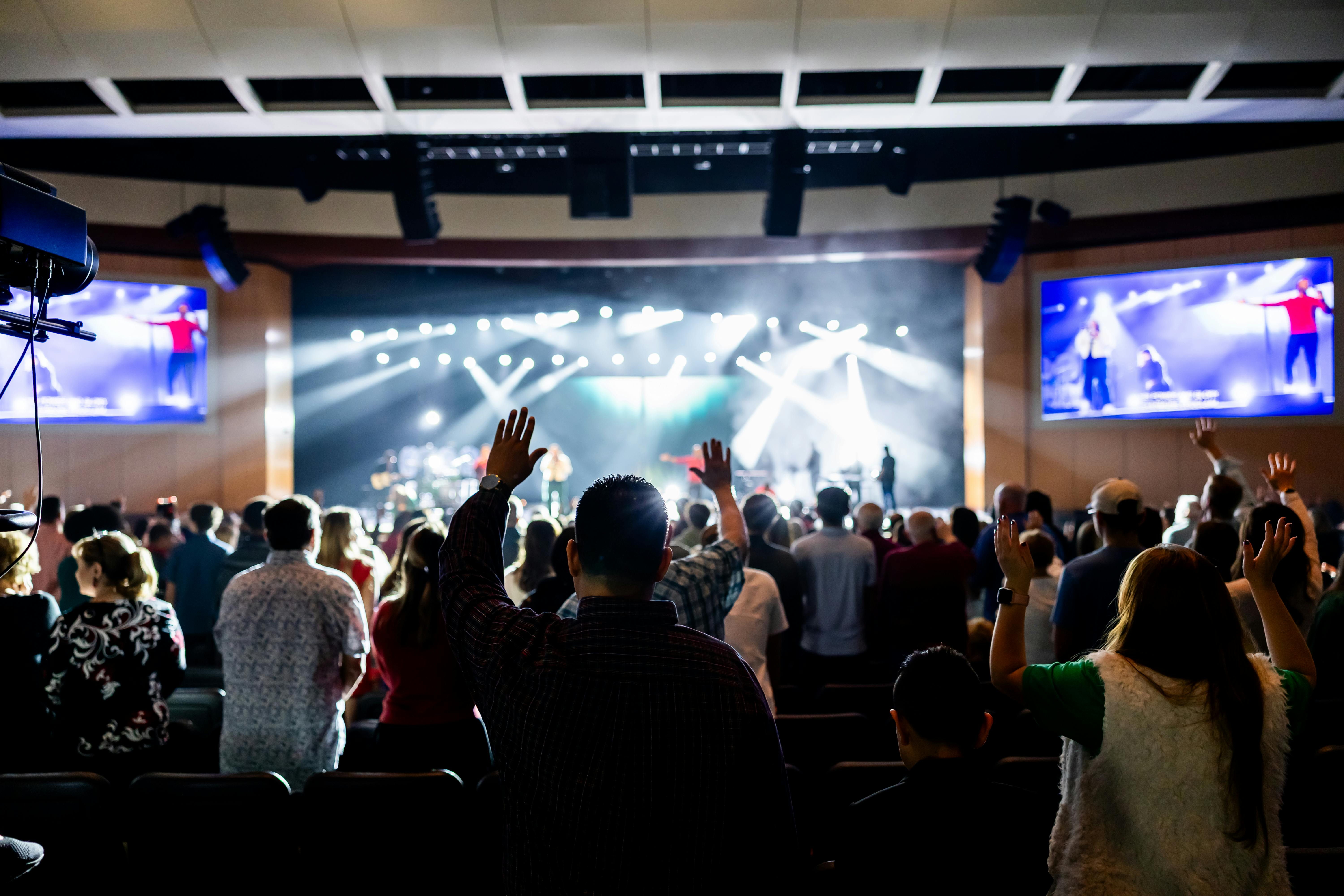 Ücretsiz Modern bir tiyatro ortamında gerçekleşen canlı konseri coşkulu bir kalabalık, ellerini heyecanla havaya kaldırarak izliyor. Stok Fotoğraflar