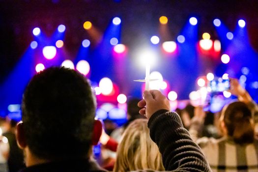 A person raising a candle in a vibrant concert-like setting with colorful lights.