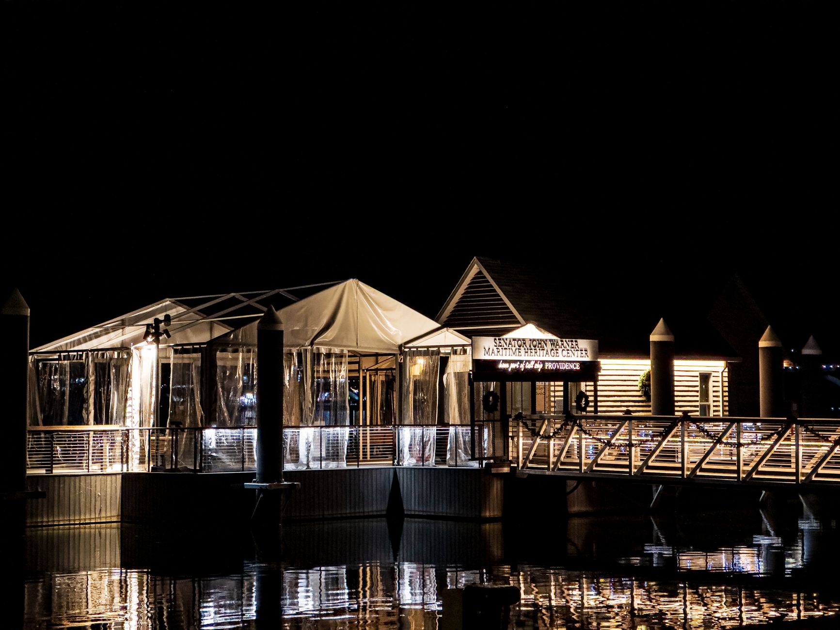 A beautifully lit maritime center at night, reflecting on calm water.