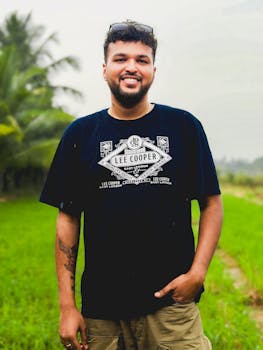 Casual portrait of a smiling man standing in a green outdoor landscape.
