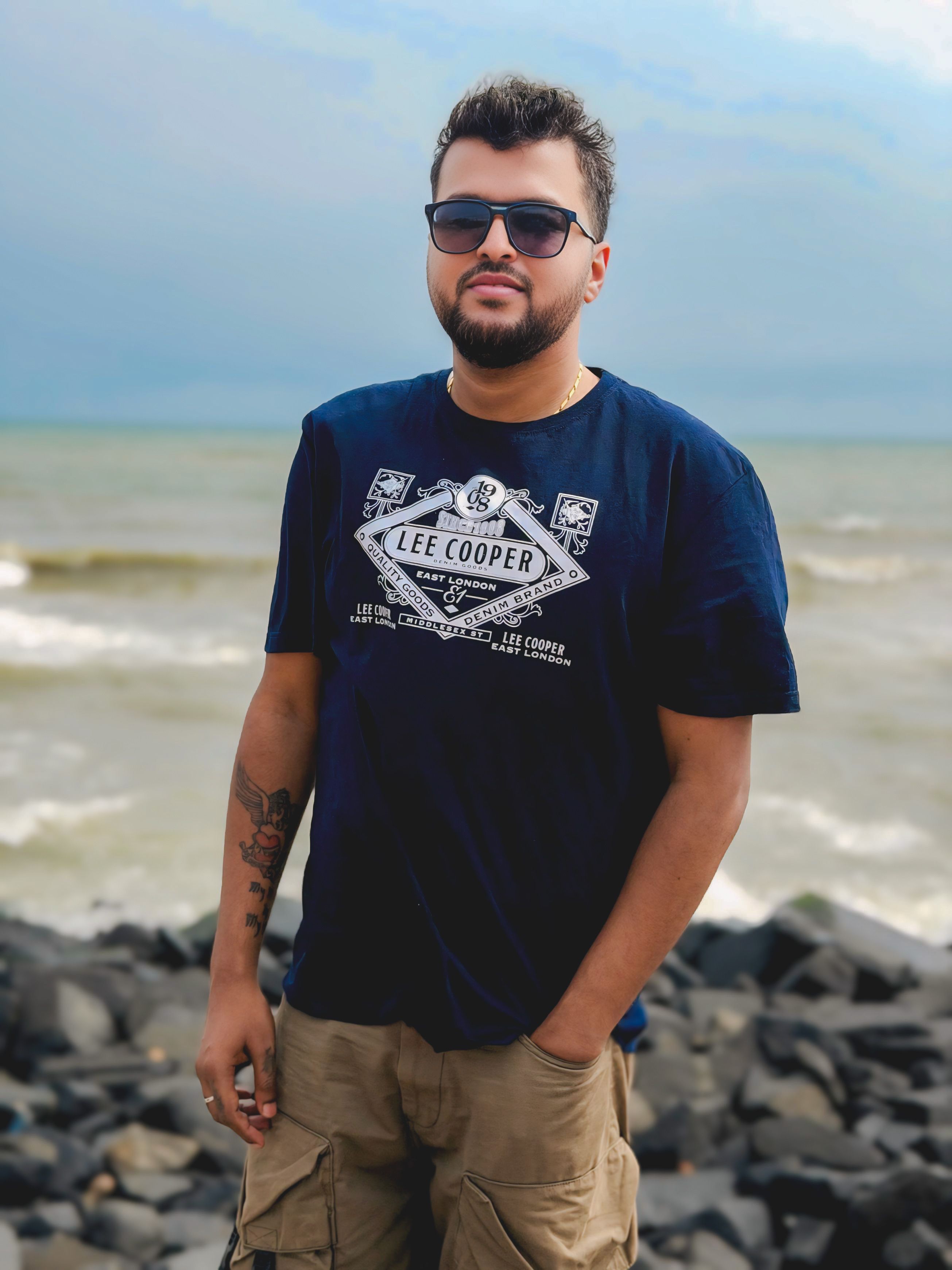 Portrait of a man in casual attire standing on a rocky beach with waves in the background.