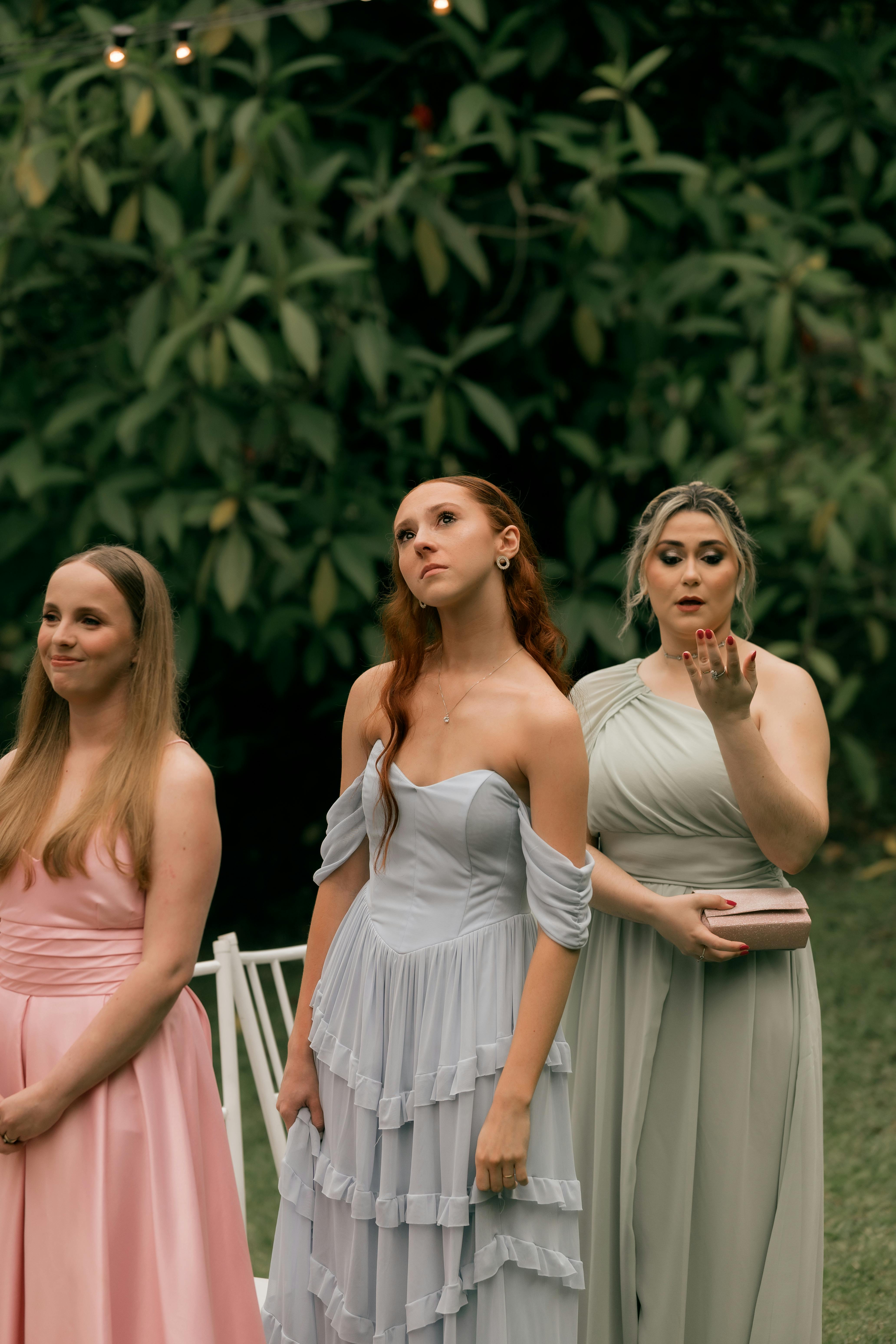 Gratis Tres damas de honor con vestidos pastel disfrutan de una boda al aire libre, mostrando una moda elegante y expresiones alegres. Foto de stock