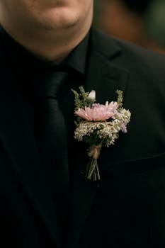 Close-up of a man wearing a black suit with a pink floral boutonniere, perfect for weddings.