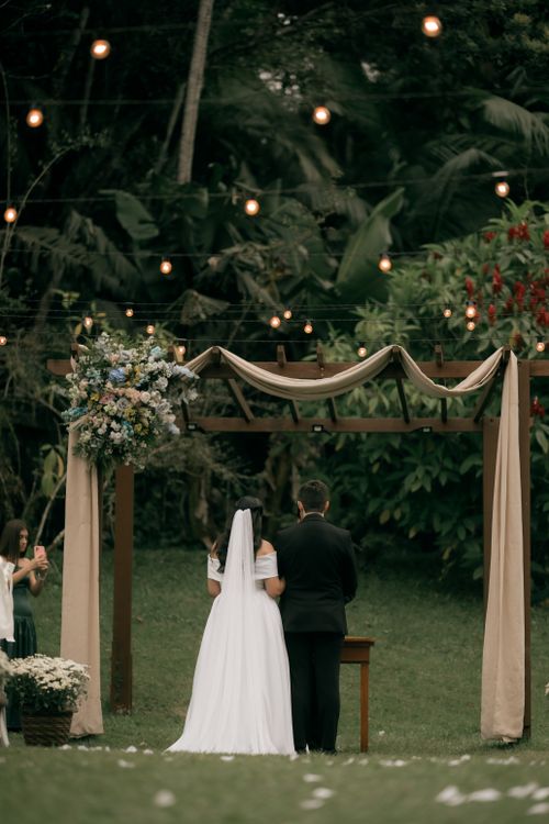 Free A couple getting married under a beautifully decorated arch in a garden. Stock Photo