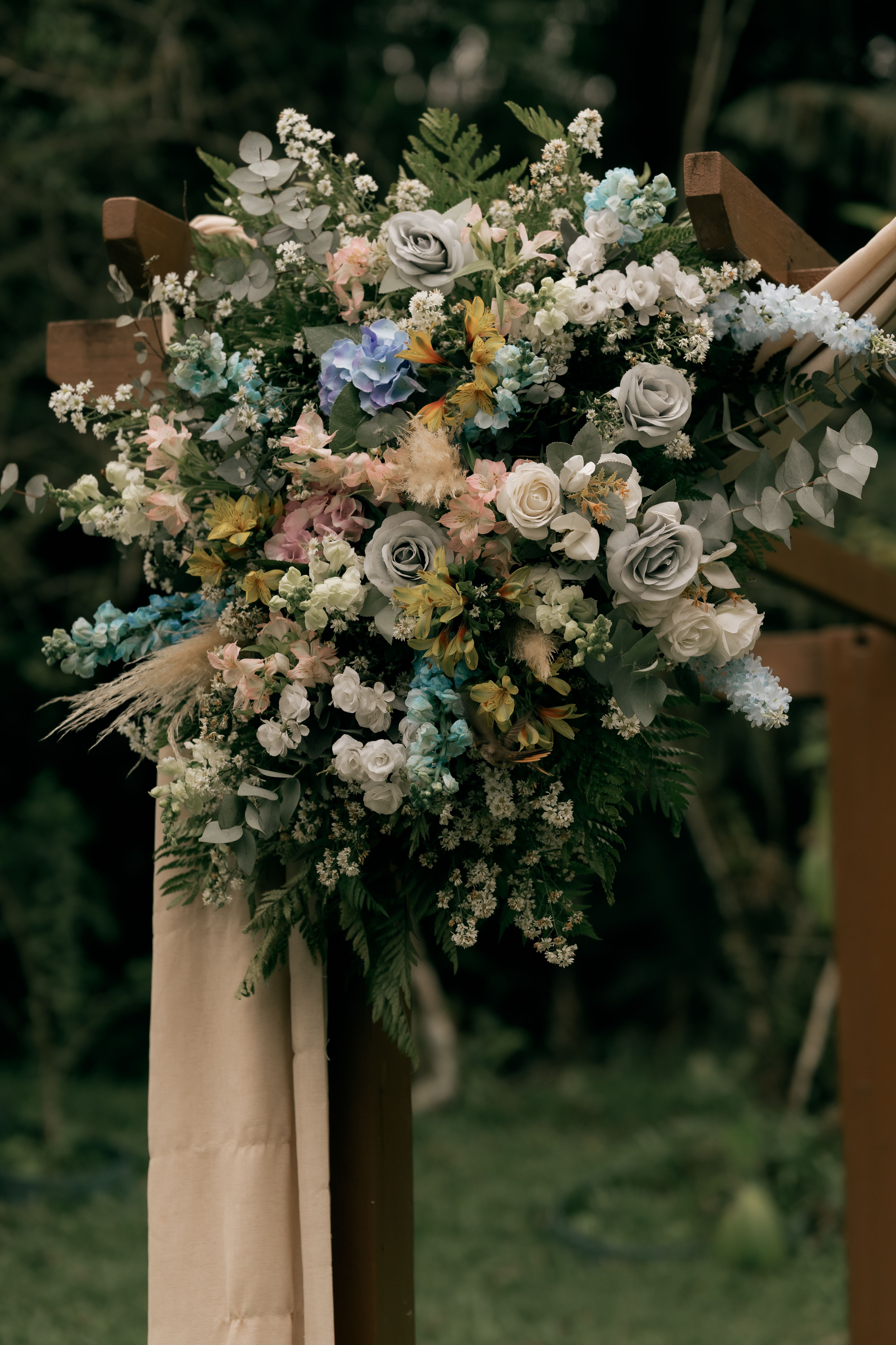 [ColoSach]-beautiful-floral-arrangement-featuring-roses-and-greenery-on-a-wooden-arch-outdoors.
