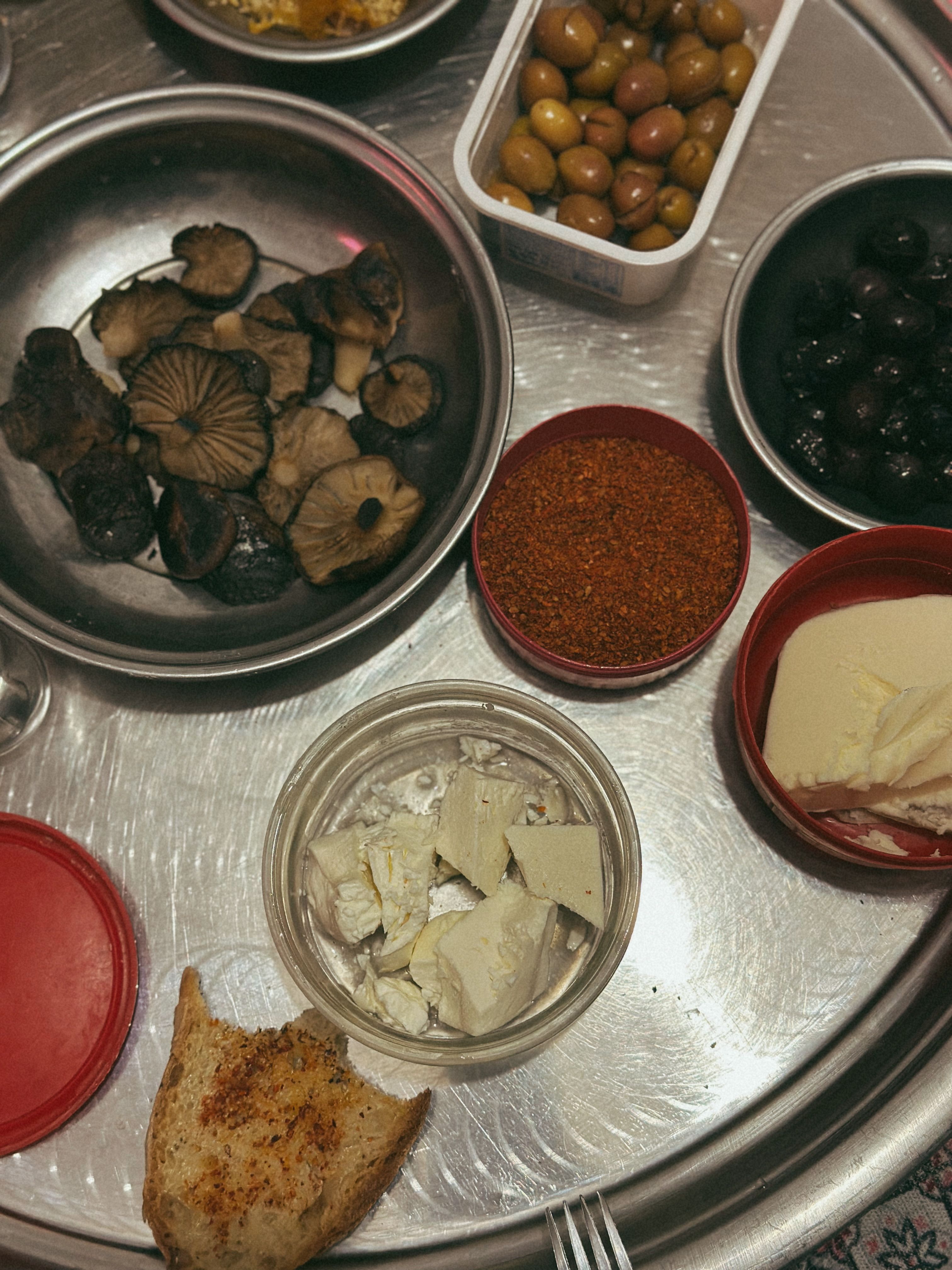A variety of Mediterranean appetizers including olives, cheese, and mushrooms served on a tray.