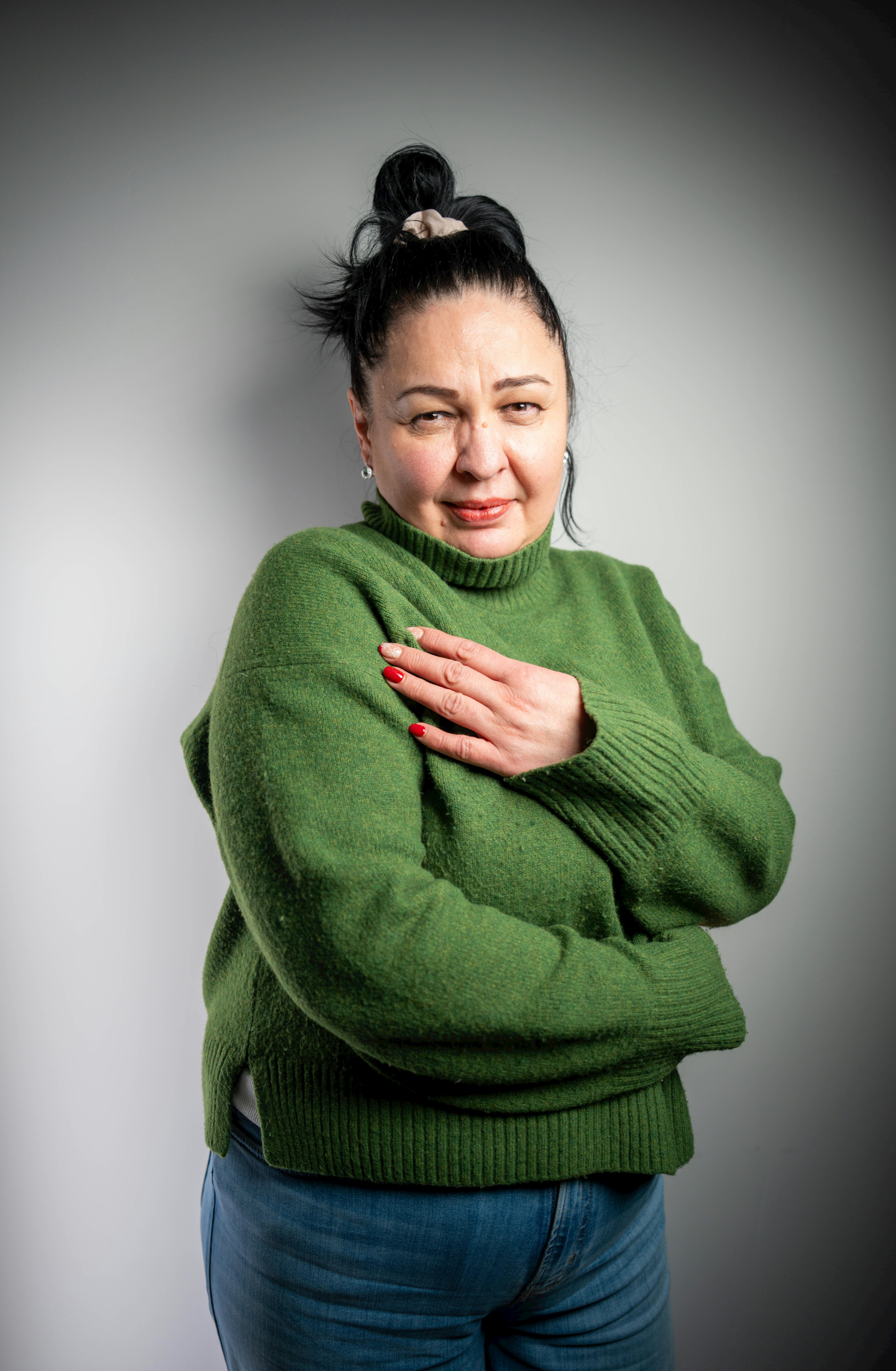 Gratis Una mujer elegante con un suéter verde posa con confianza en un interior contra un fondo neutro. Foto de stock