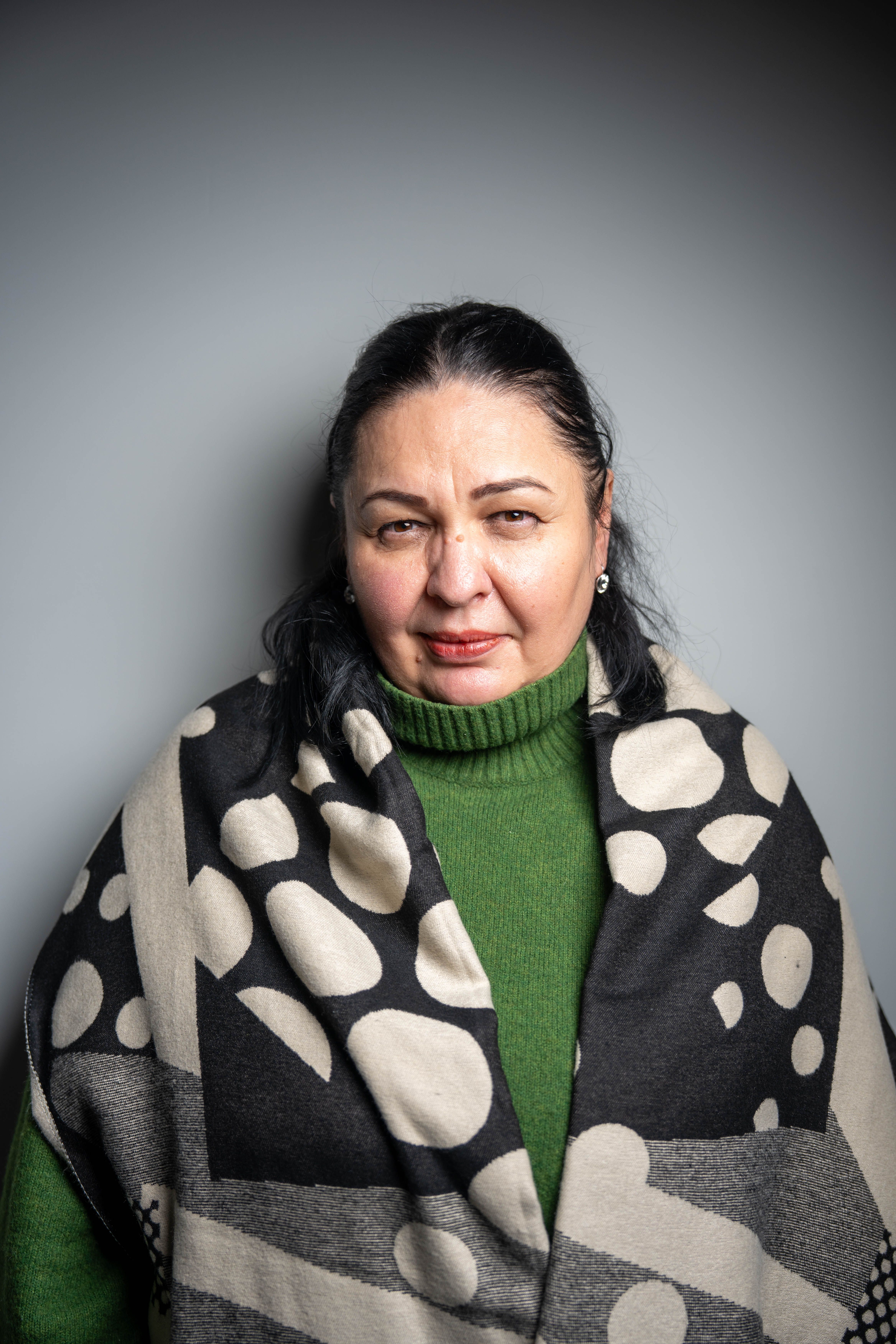 Middle-aged woman wearing a stylish shawl and green sweater against a gray background.