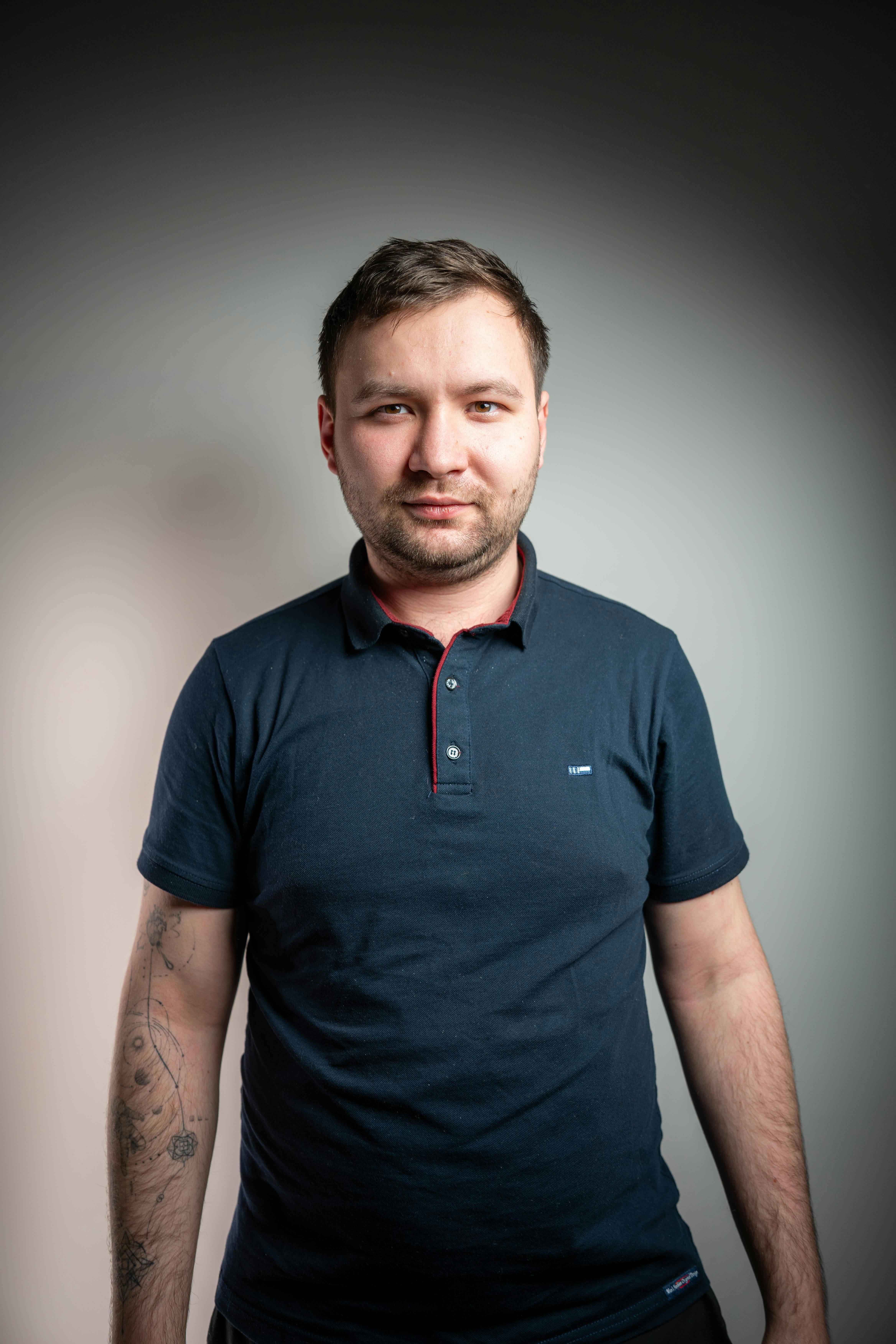 Studio portrait of a man with short hair in a navy polo shirt against a gradient background.
