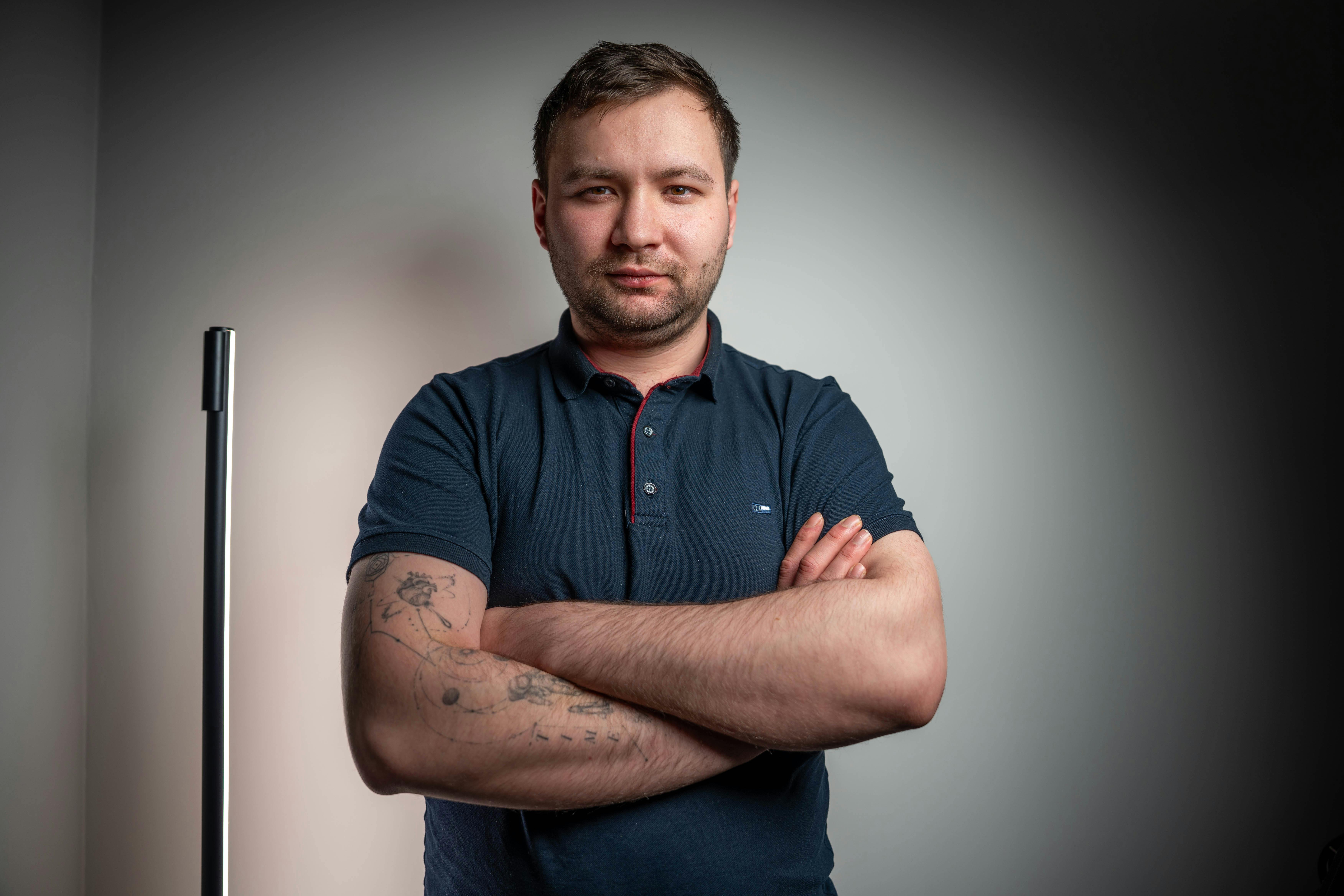 Gratis Portrett av en selvsikker voksen mann med kryssede armer og tatoveringer i et studiomiljø. Arkivbilde