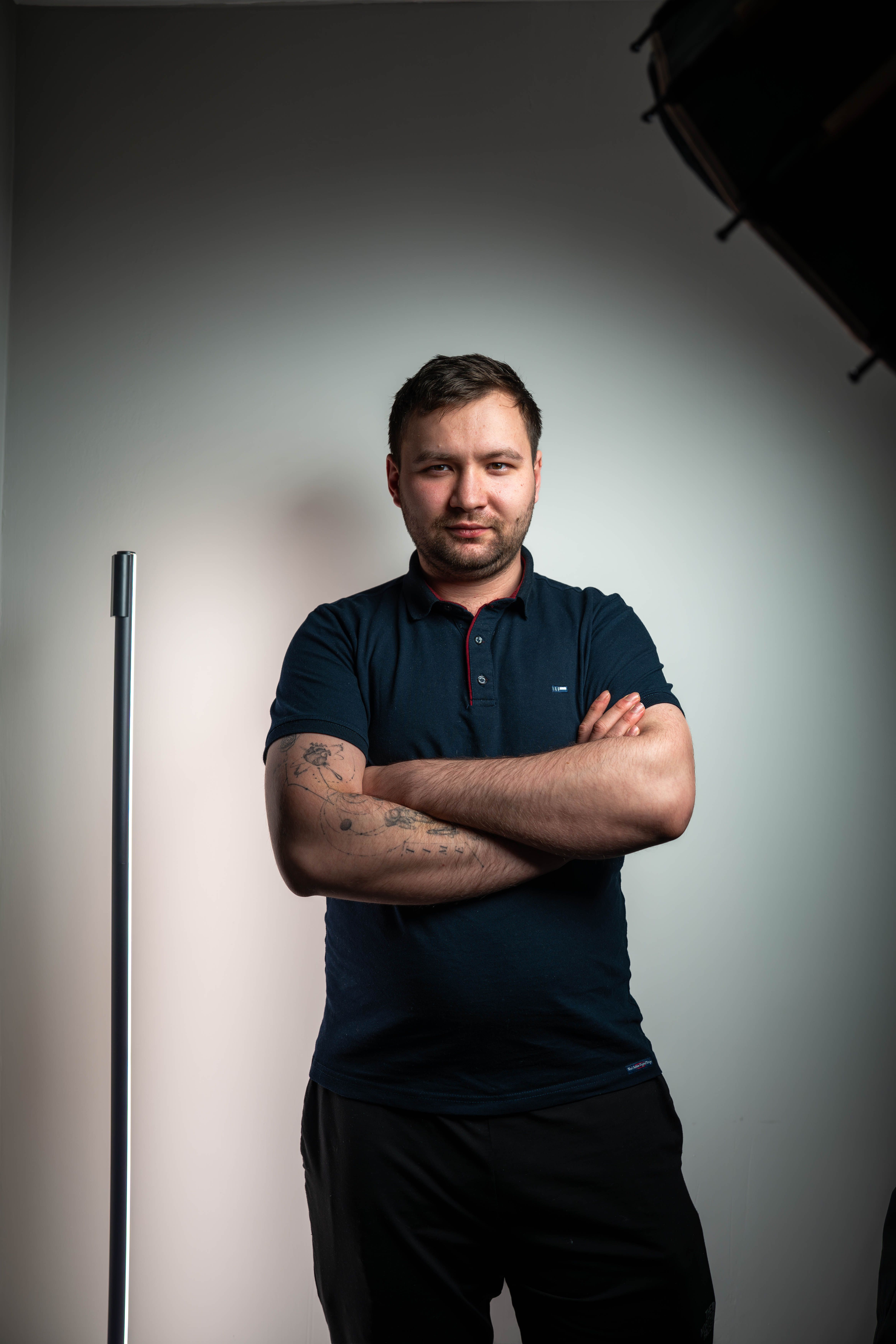 Portrait of a confident man with tattoos standing in a studio, arms crossed.