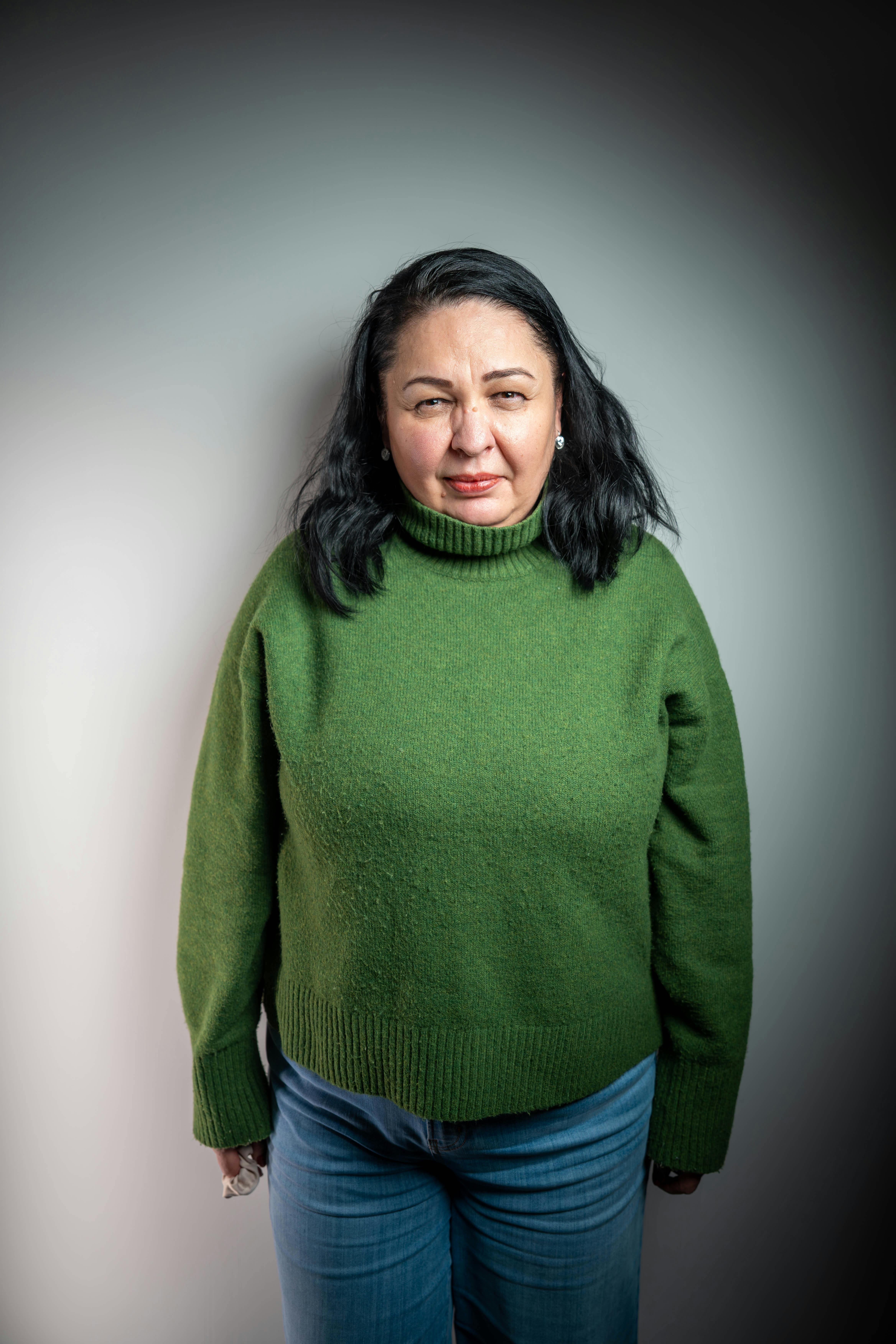 Gratis Retrato de una mujer adulta posando en el interior, vistiendo un suéter verde y jeans. Foto de stock