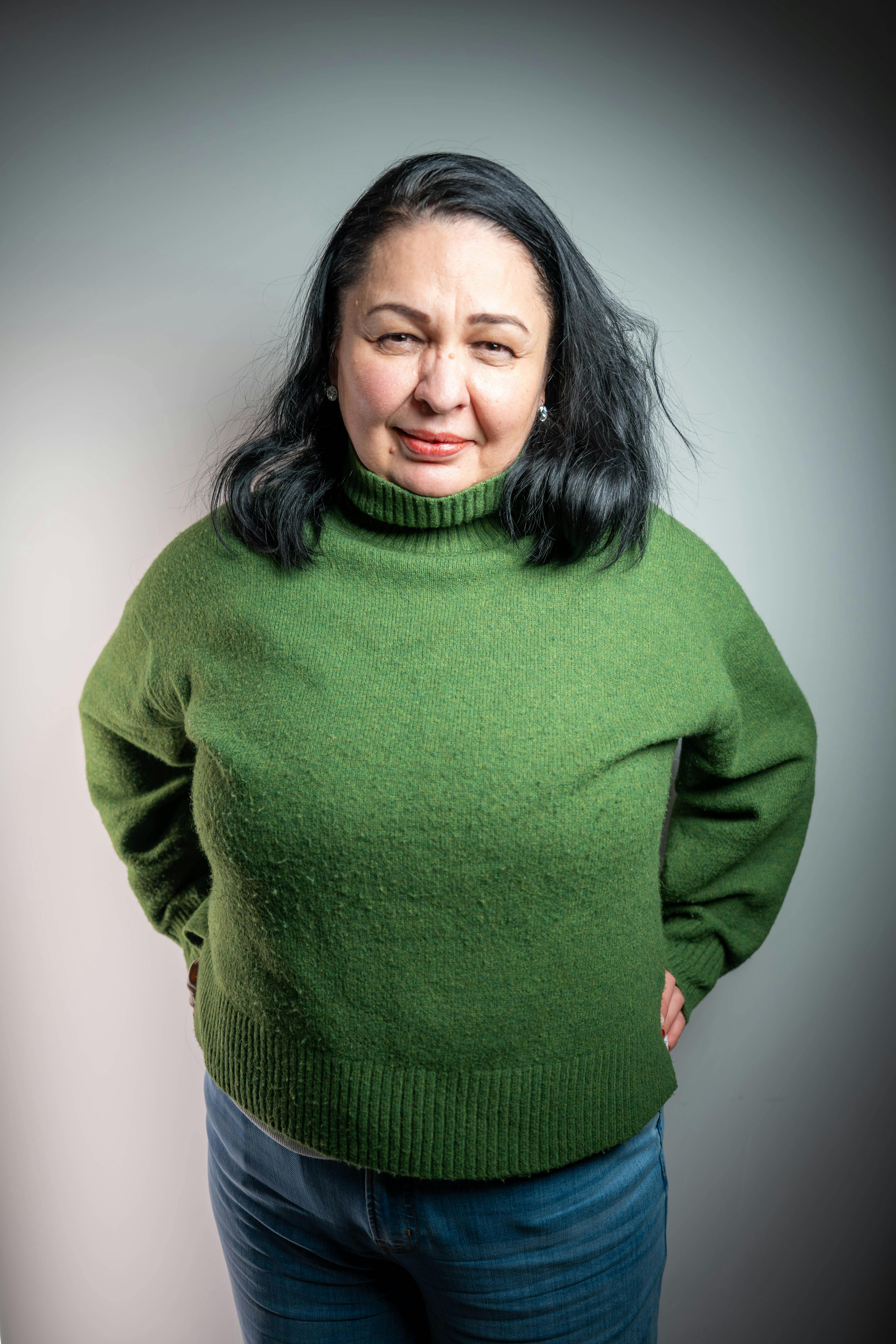 grátis Mulher confiante, vestindo um suéter verde, posando em ambiente interno contra um fundo liso. Foto profissional