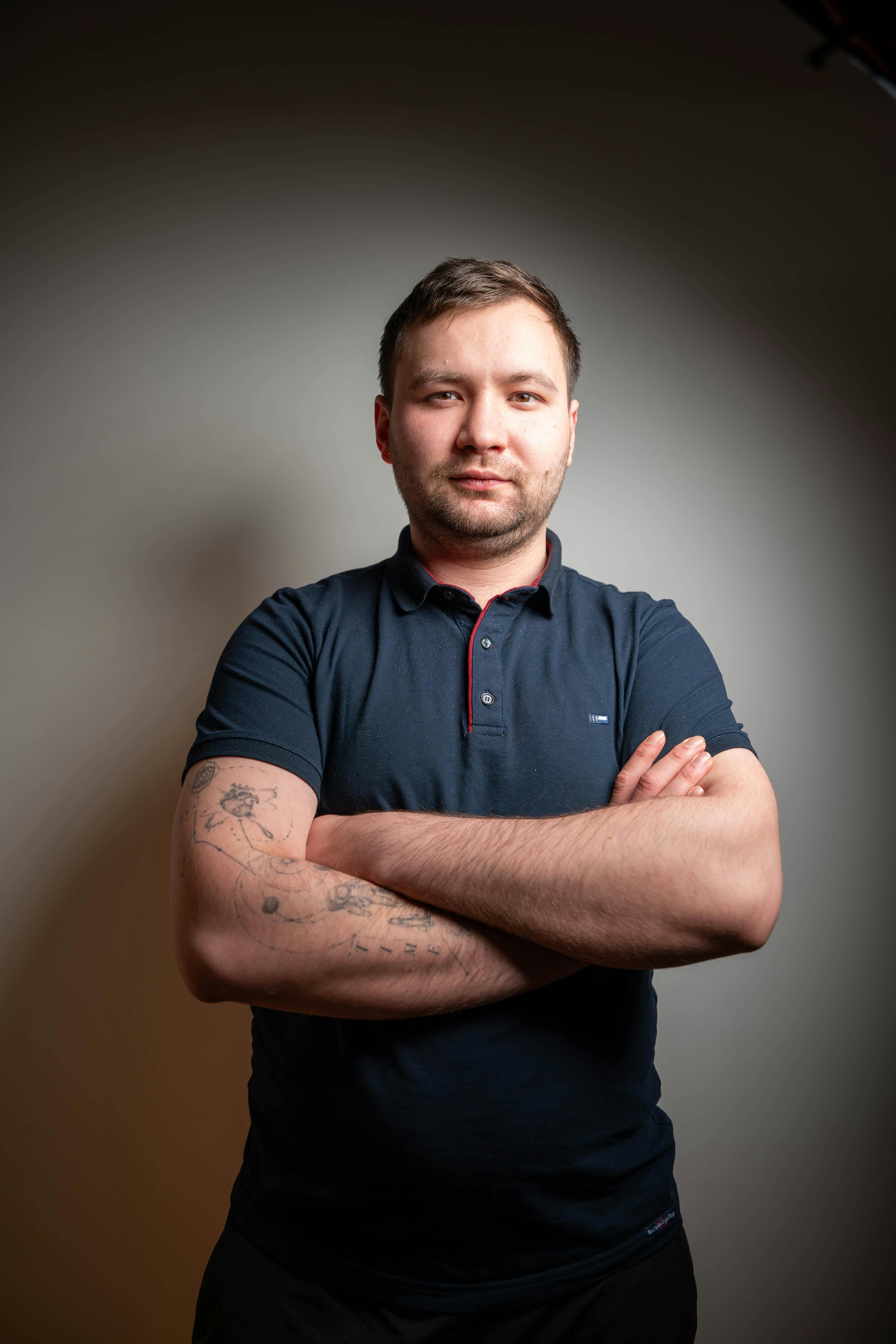 Gratis Retrato de un joven confiado con tatuajes de pie en un interior contra un fondo neutro. Foto de stock