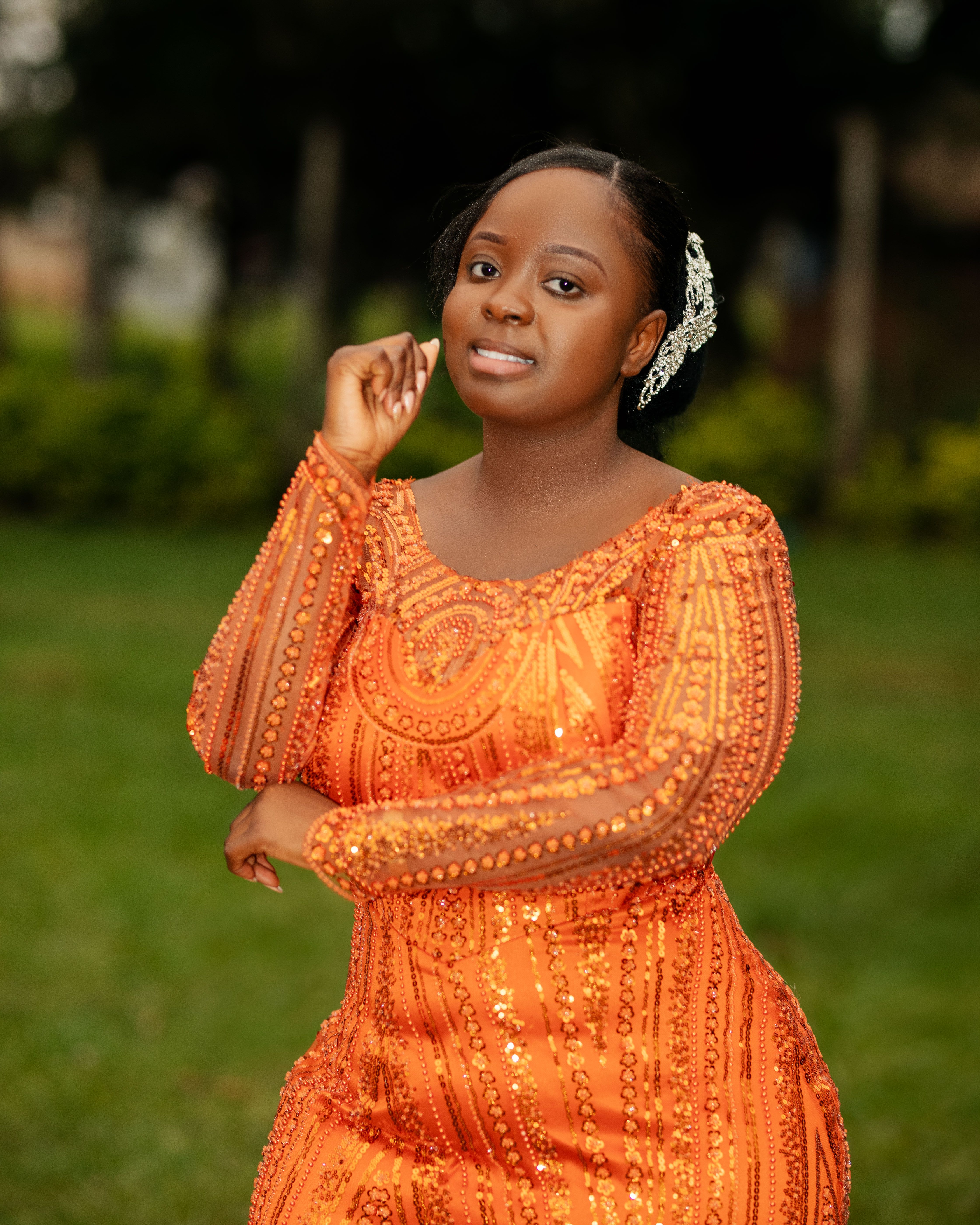 A woman poses gracefully in a sequined orange dress, outdoors. Bright and elegant.