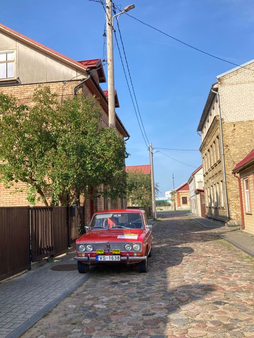 Free A vintage red car parked on a quaint cobblestone street on a sunny day, exuding nostalgic charm. Stock Photo