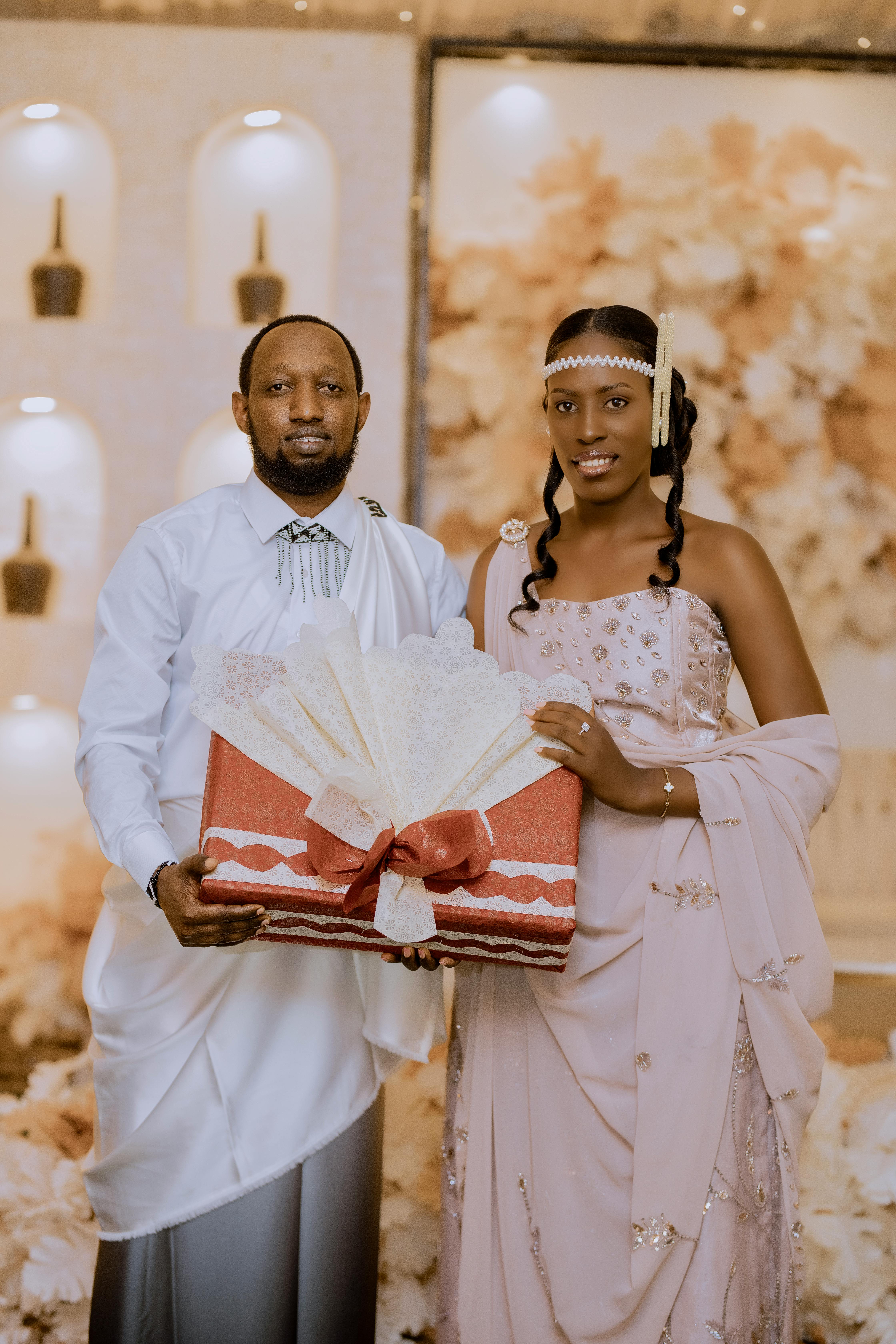 Gratis Elegante pareja vestida formal sosteniendo un regalo en un entorno interior decorativo, perfecto para ocasiones festivas. Foto de stock