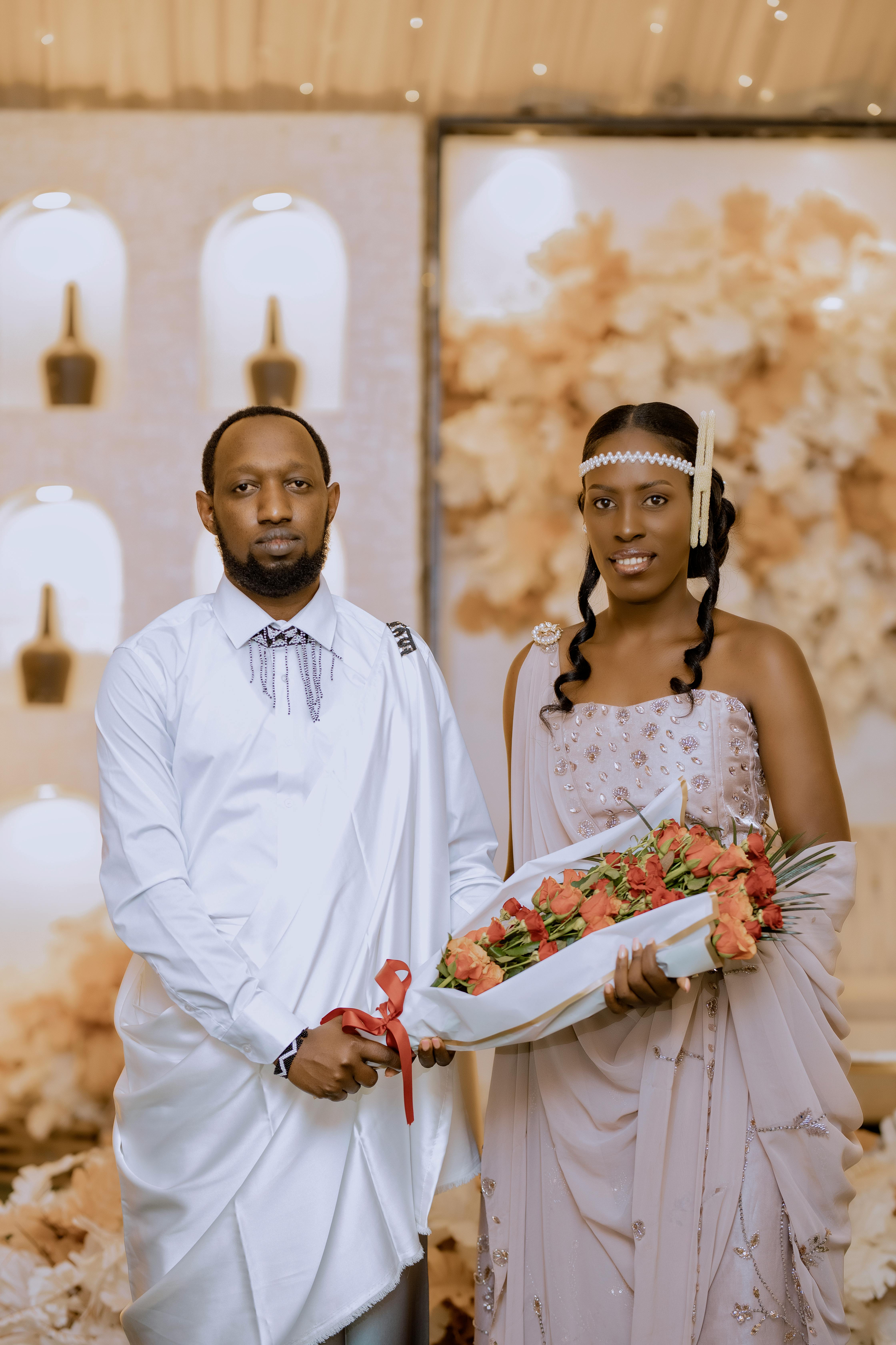 Gratis Novia y novio con atuendo tradicional sosteniendo flores en una ceremonia en el interior. Foto de stock