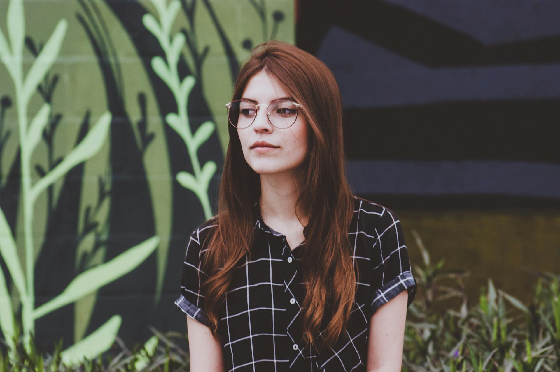 Portrait of a young woman in glasses standing outdoors against a mural background.