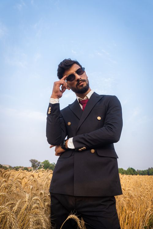 Free A fashionable man in a suit posing confidently in a wheat field under a clear sky. Stock Photo