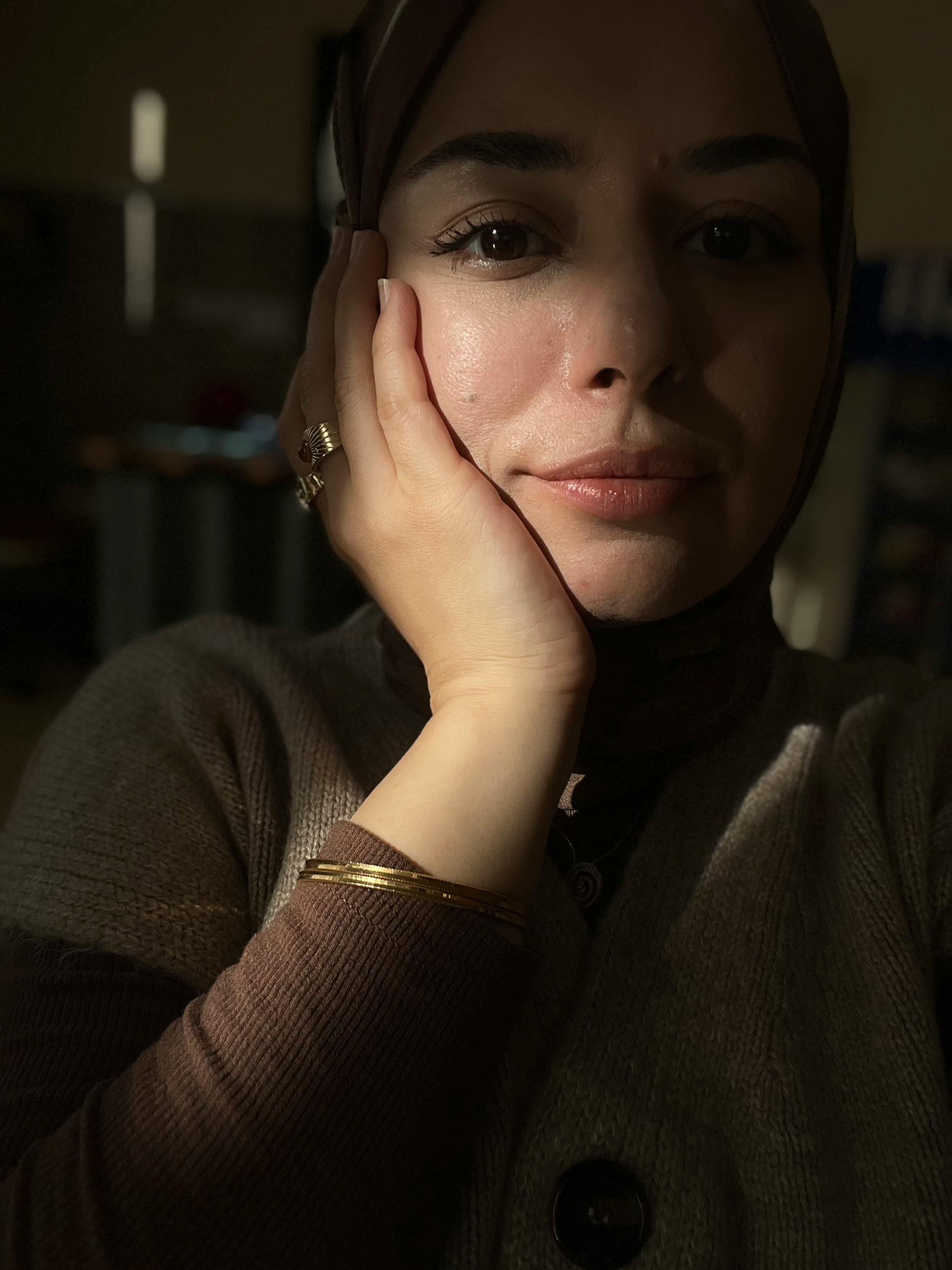 Gratis Una mujer reflexiva bajo una suave iluminación interior, vistiendo un hijab y reflejando su estado de ánimo. Foto de stock