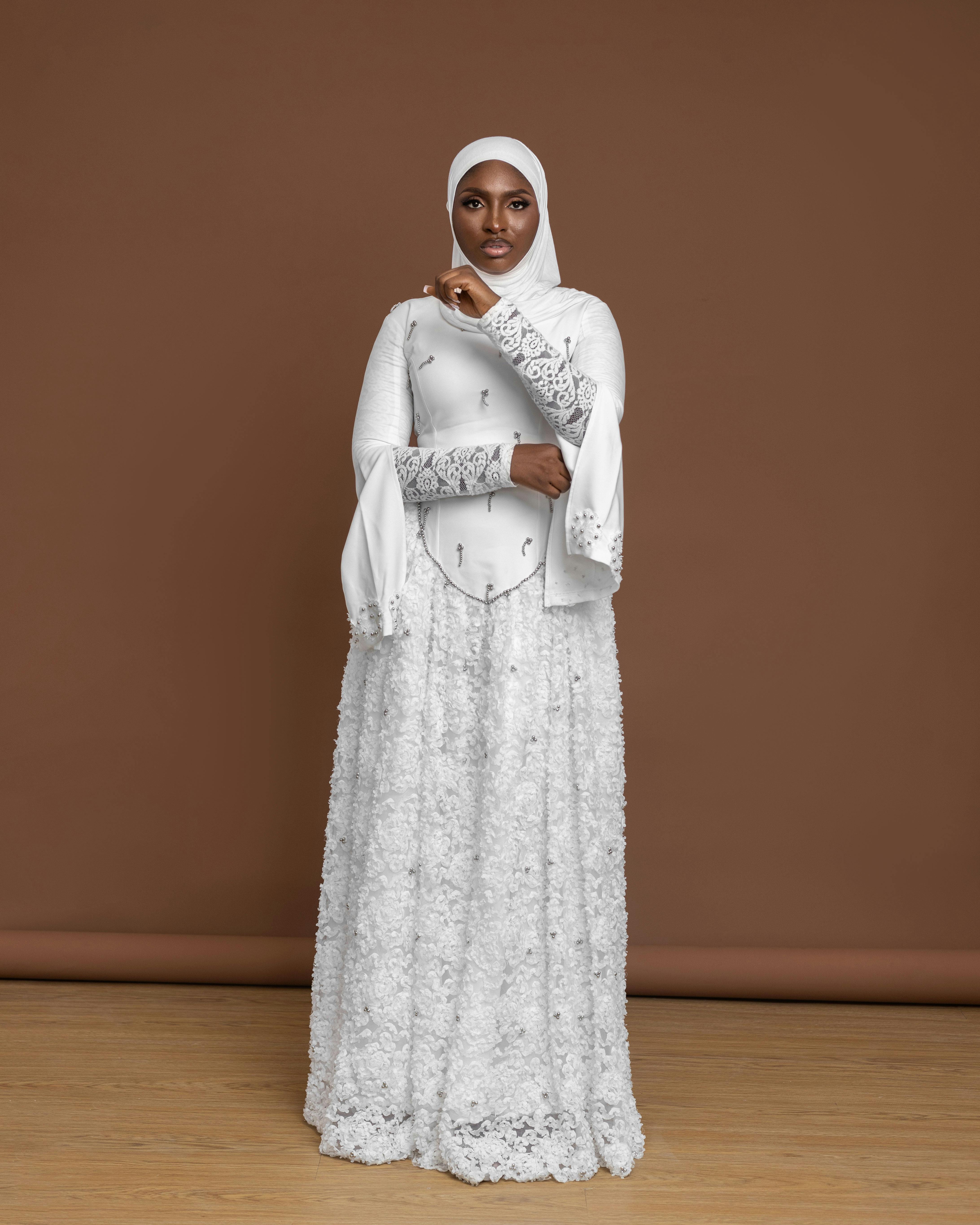 Gratis Mujer elegante con un hijab blanco y un vestido posando sobre un fondo marrón. Foto de stock