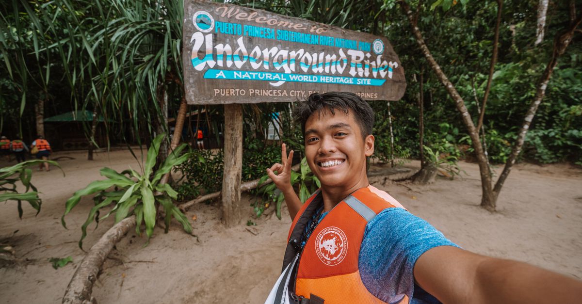 Young man taking a selfie at Puerto Princesa Underground River sign in Palawan, Philippines.