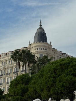 View of the Carlton Hotel in Cannes surrounded by lush greenery and palm trees.