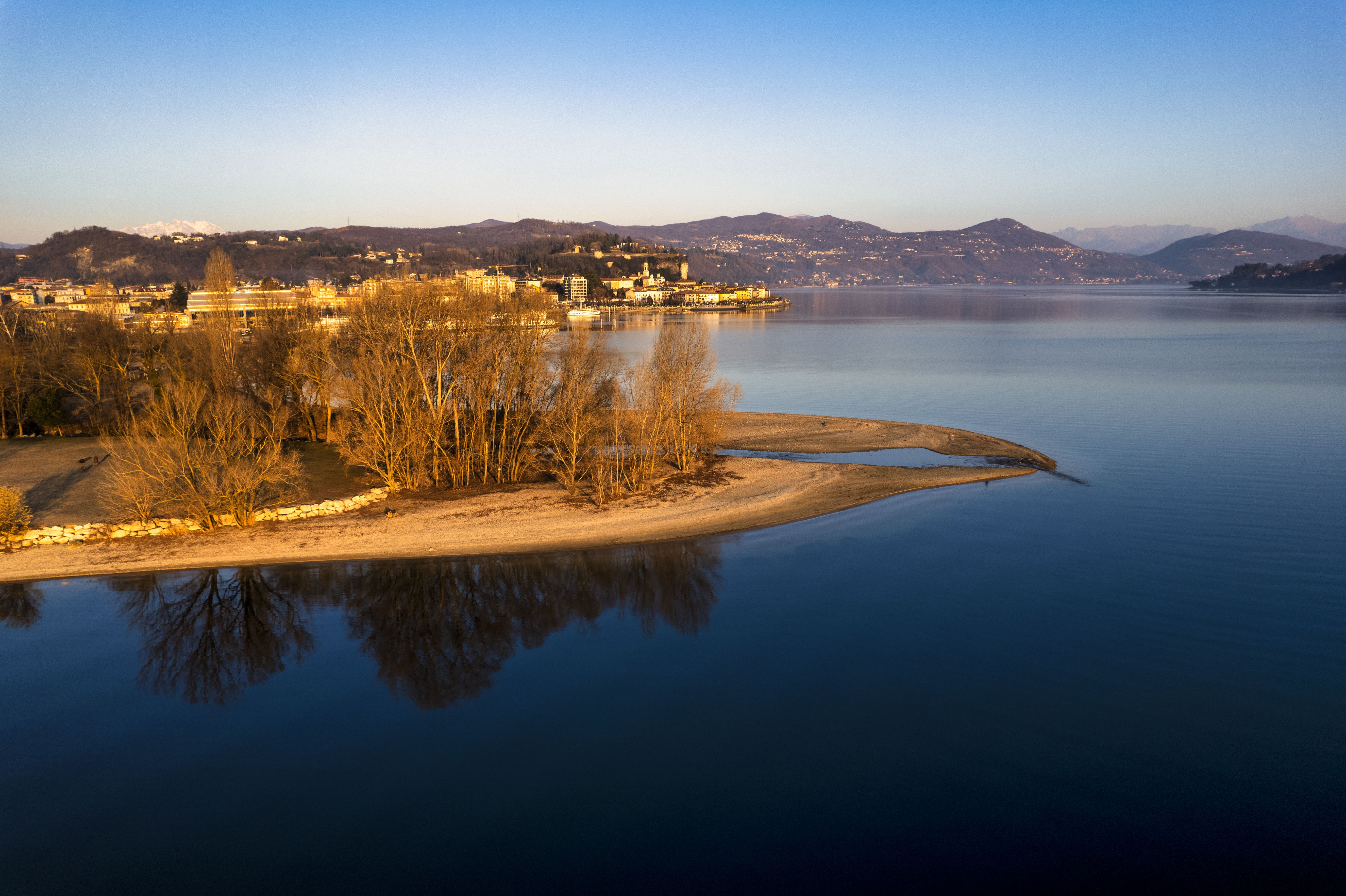 A serene aerial view of Lake Maggiore with reflections, captured at sunset with surrounding hills.