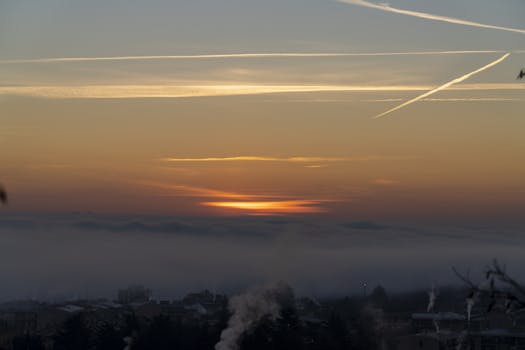 A beautiful sunrise over a cityscape shrouded in fog with visible vapor trails.