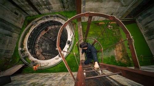 Free Man ascends a rusty ladder inside an abandoned industrial site. Urban exploration vibe. Stock Photo