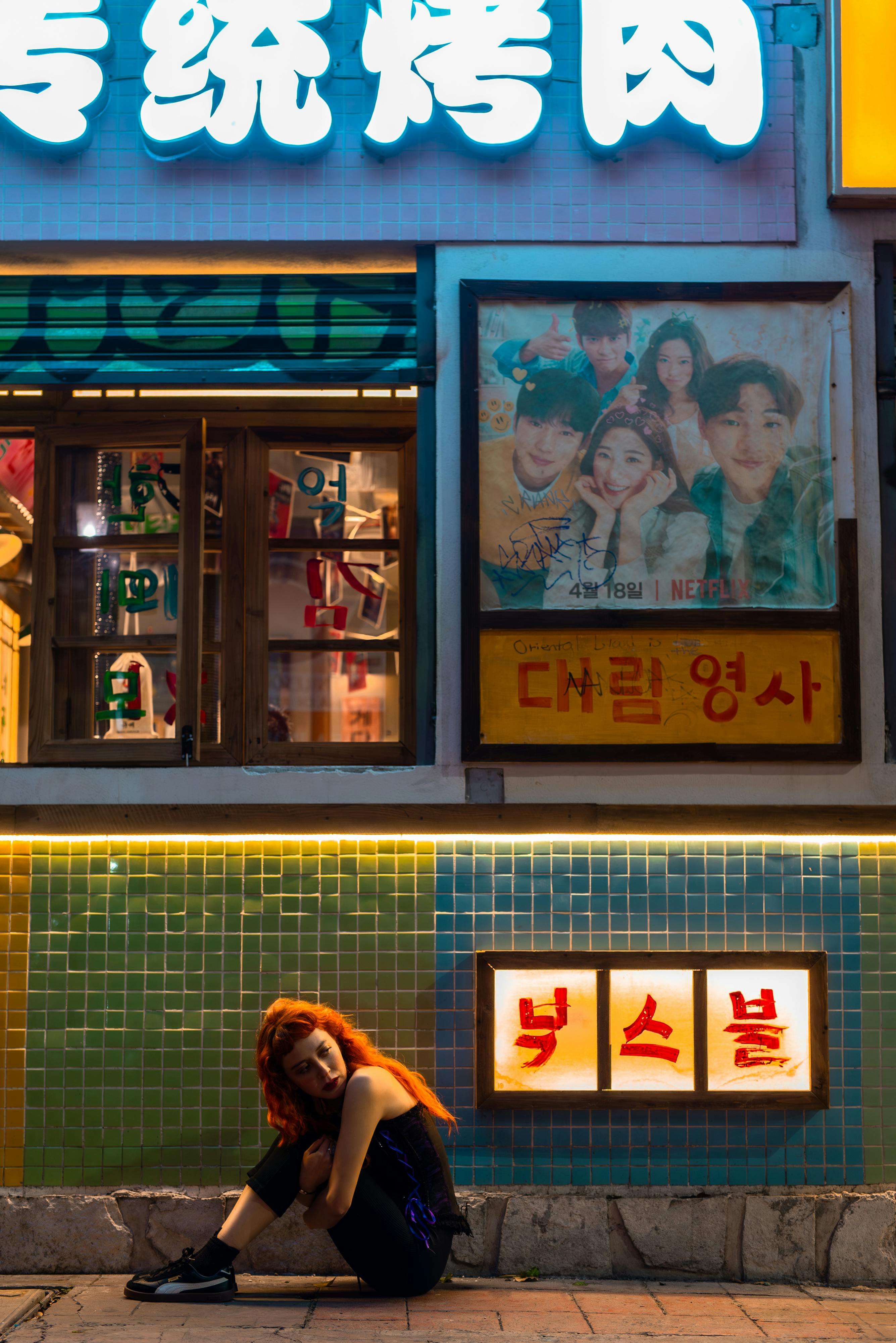 Gratuit Une personne aux cheveux d'un roux flamboyant est assise devant une boutique colorée, de nuit, au Mexique. Photos