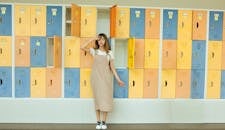 在室内学校环境中，一位时尚女性穿着休闲时装，对着充满活力的储物柜摆姿势