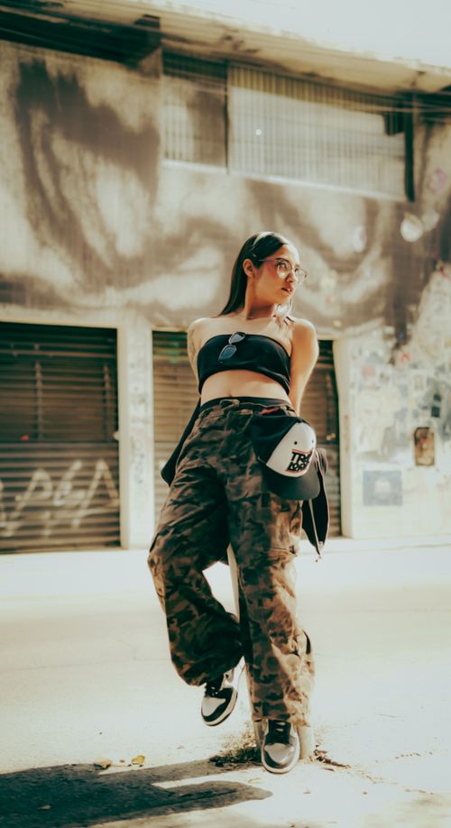 Free A stylish woman in camo pants stands confidently in a graffiti-decorated urban alley. Stock Photo
