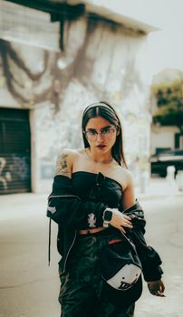 Confident young woman in streetwear, posing confidently in an urban graffiti backdrop, embodying modern urban style.