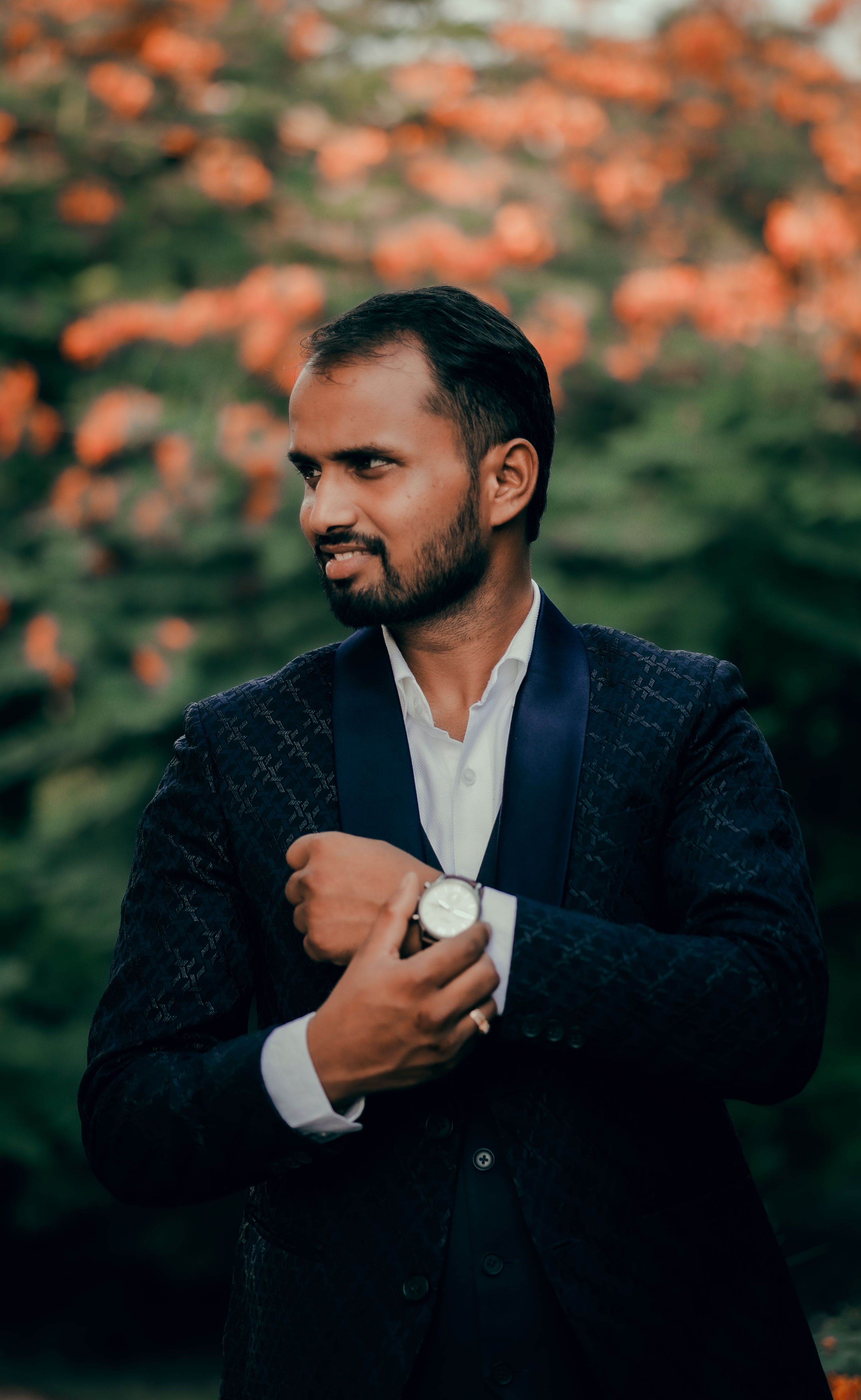 Confident man adjusting his watch elegantly posed against a vibrant floral background.
