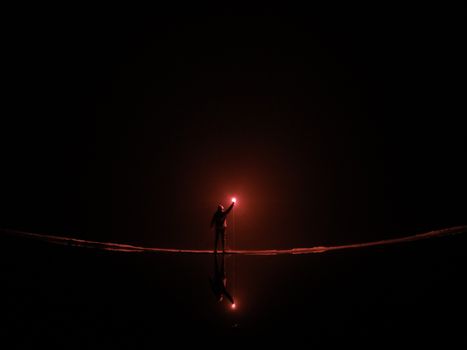 Dramatic silhouette of a person holding a flare at night, reflected on water.