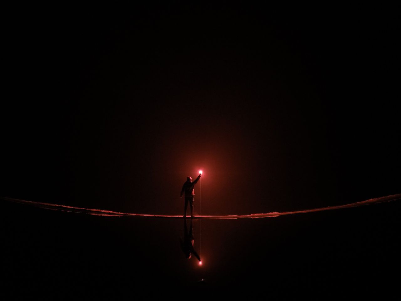 dramatic silhouette of a person holding a flare at night reflected on