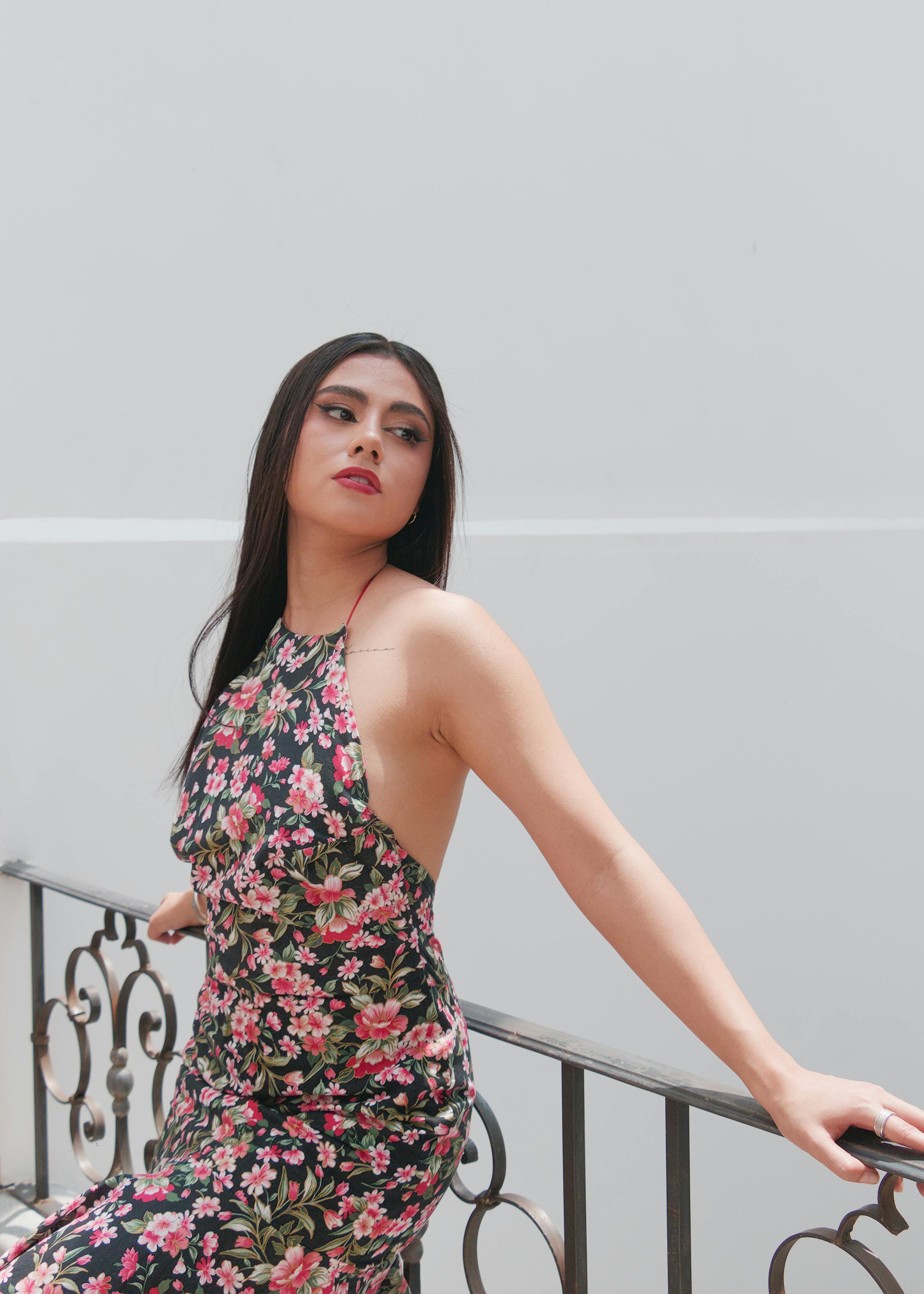 De franc Una dona elegant amb vestit floral posa elegantment en un balcó, desprèn confiança i gràcia. Foto d'estoc