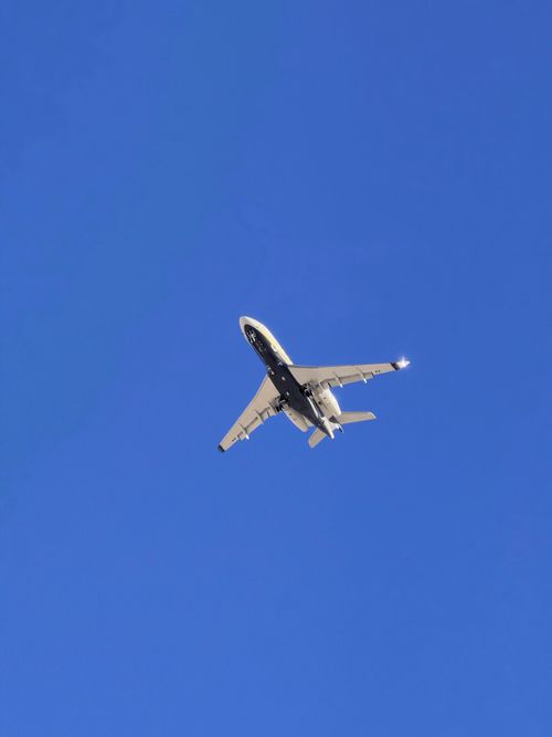 Free A commercial airplane captured mid-flight against a bright blue sky. Stock Photo