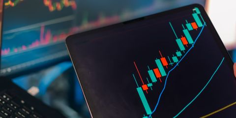 A tablet displaying a candlestick chart with a laptop screen showing stock market data for financial analysis.
